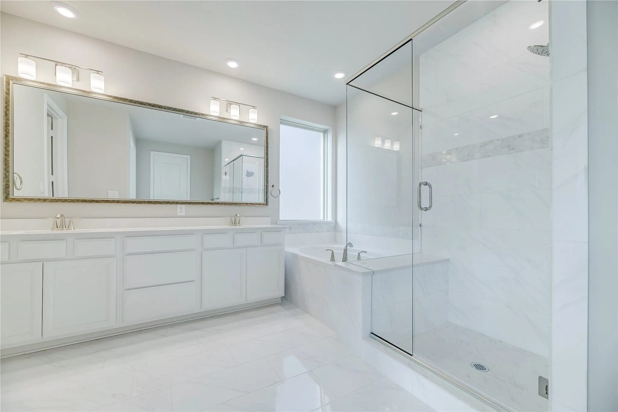 Dual vanity with white cabinetry, large framed mirror, built-in bathtub, glass-enclosed shower, and tile flooring