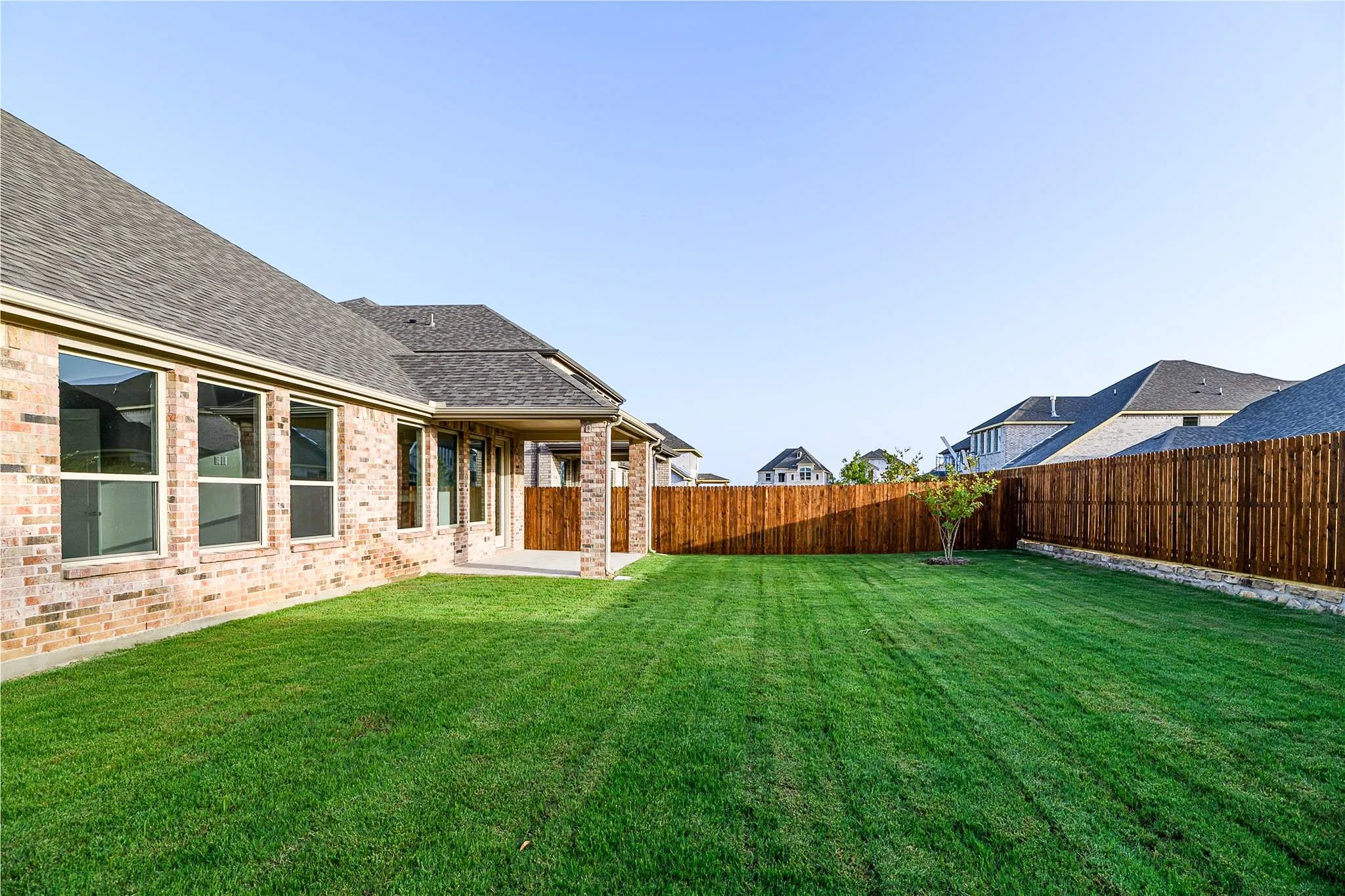 Expansive green lawn, covered patio, brick exterior, wood privacy fence, and multiple windows