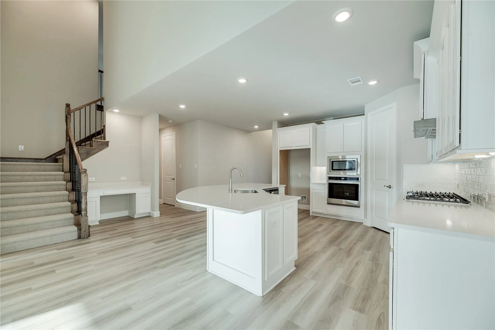 Open-concept living area with wood-finish flooring, a built-in desk, and a staircase featuring wood and metal balusters