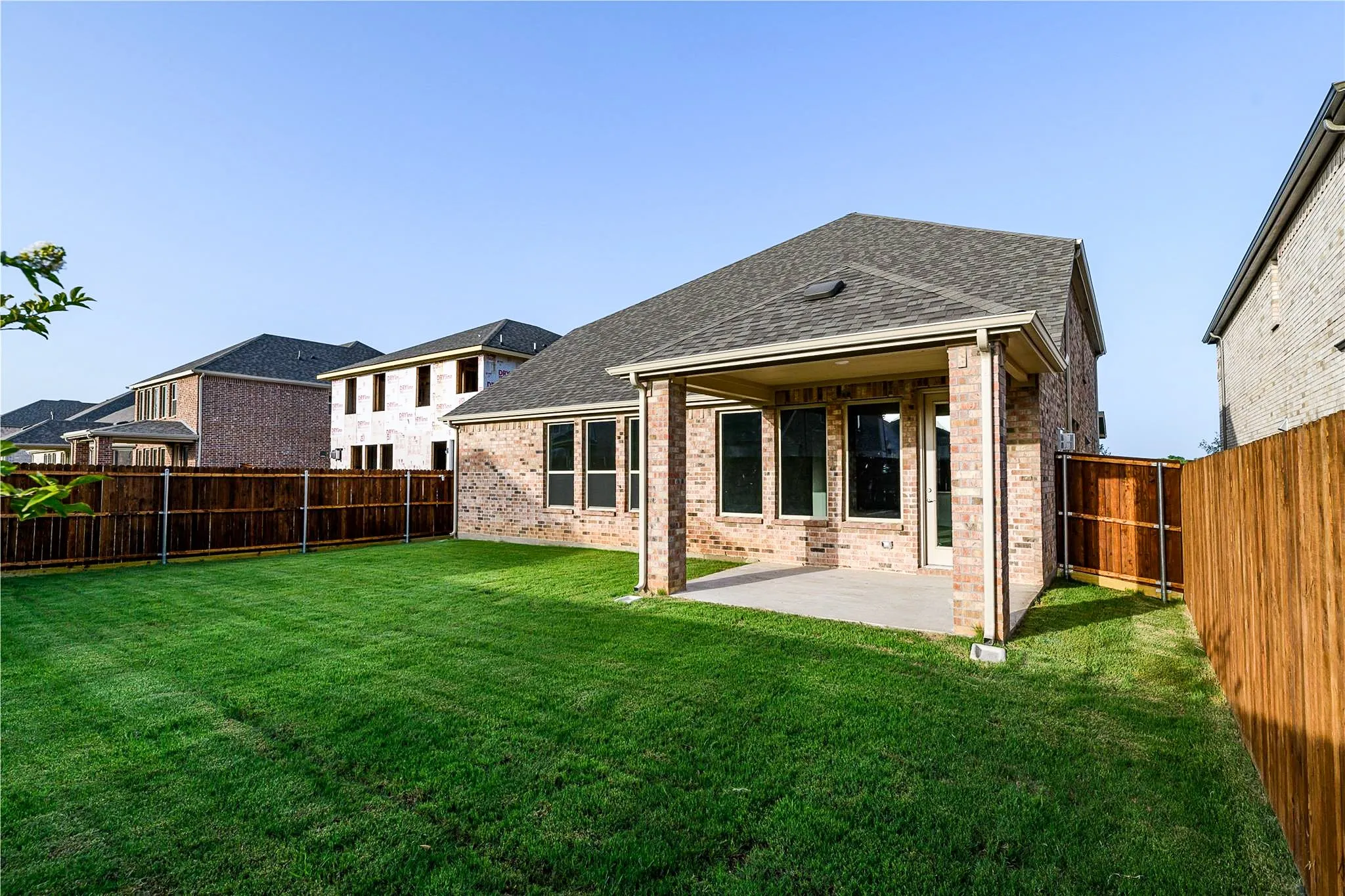 Expansive backyard featuring a manicured lawn, wood fencing, and a covered concrete patio