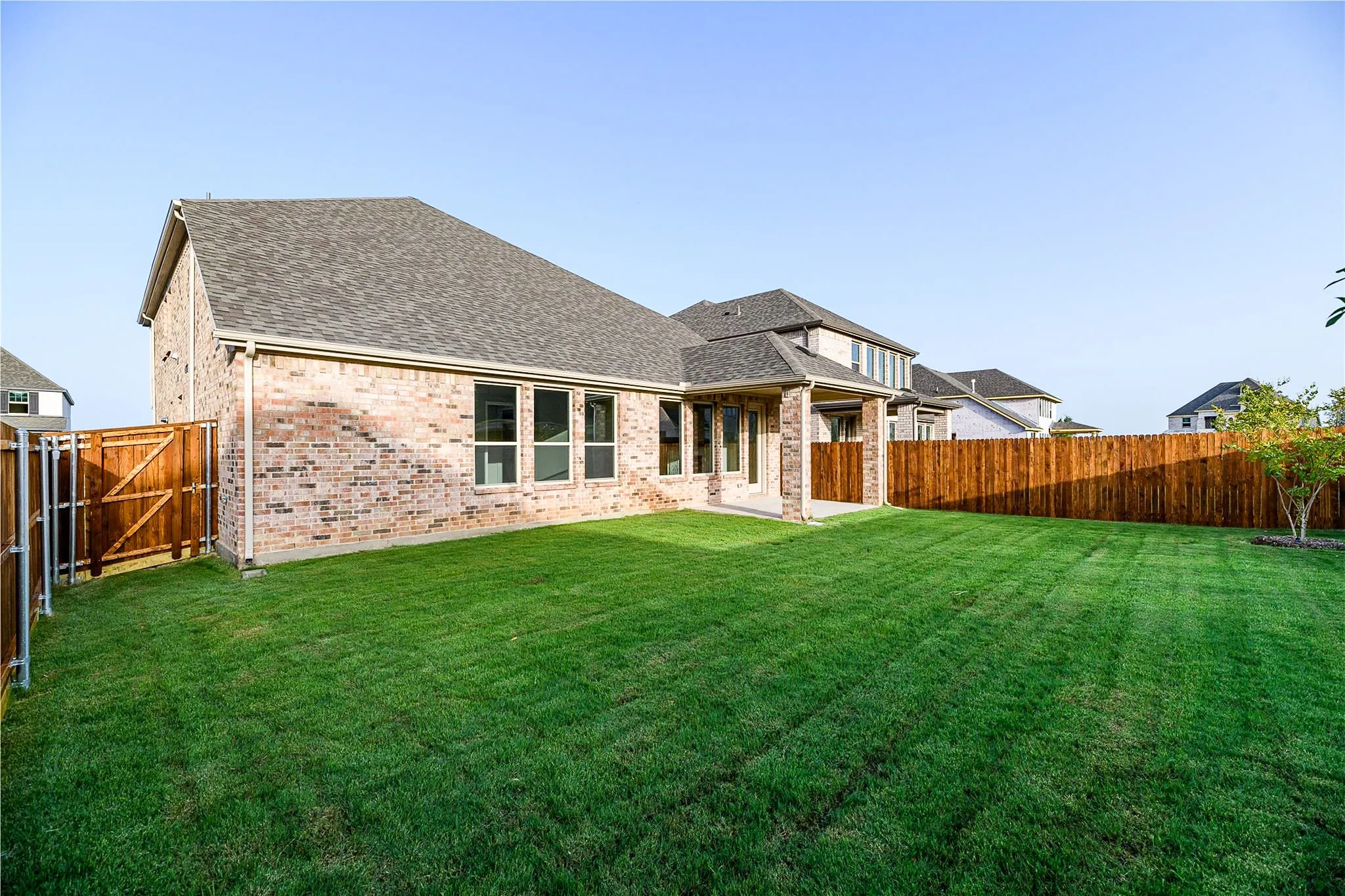 Expansive backyard featuring a manicured lawn, brick exterior, full wood privacy fencing, and multiple windows