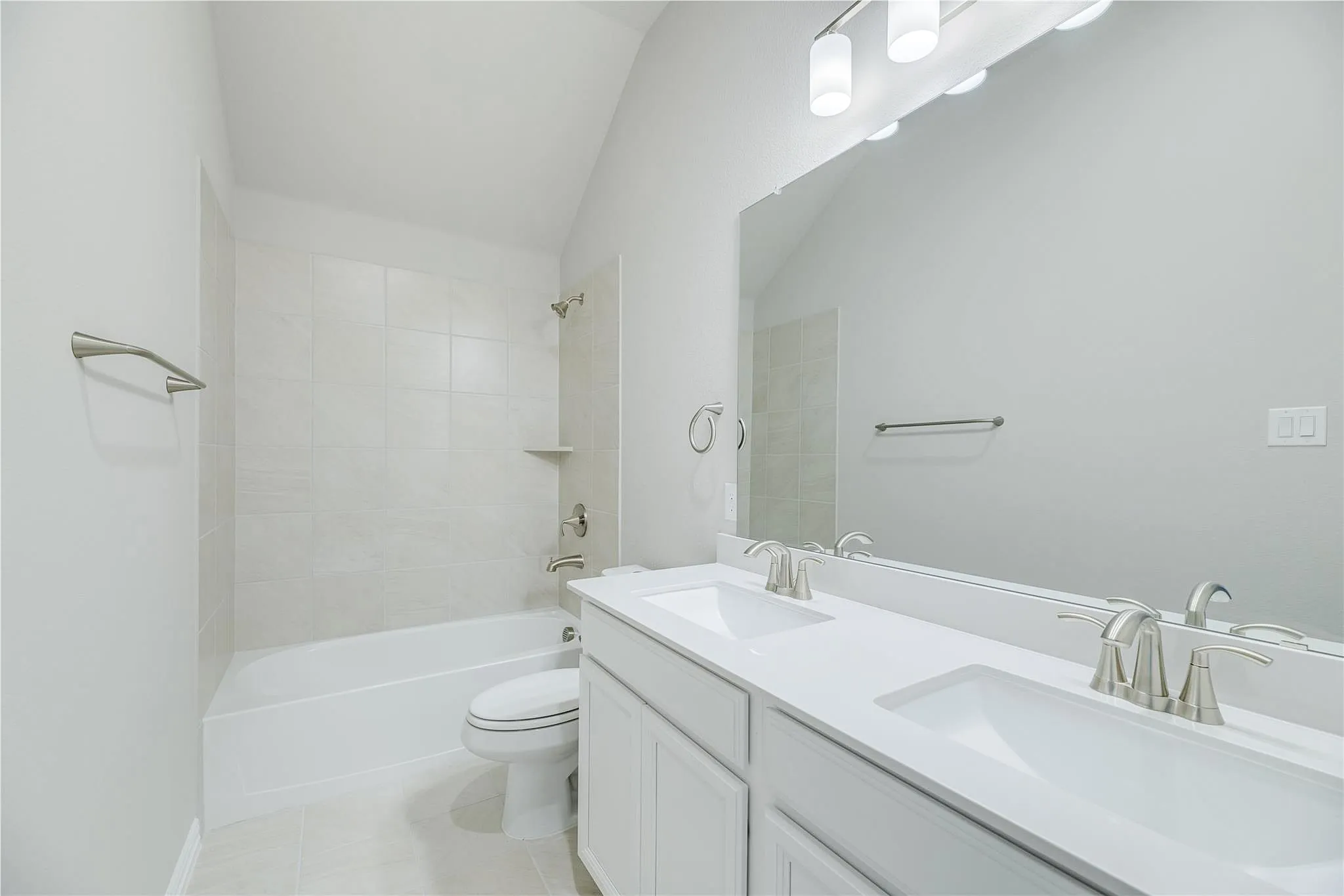 Dual vanity with integrated sinks, brushed nickel fixtures, a large wall-mounted mirror, overhead bar lighting, and a bathtub with tile surround
