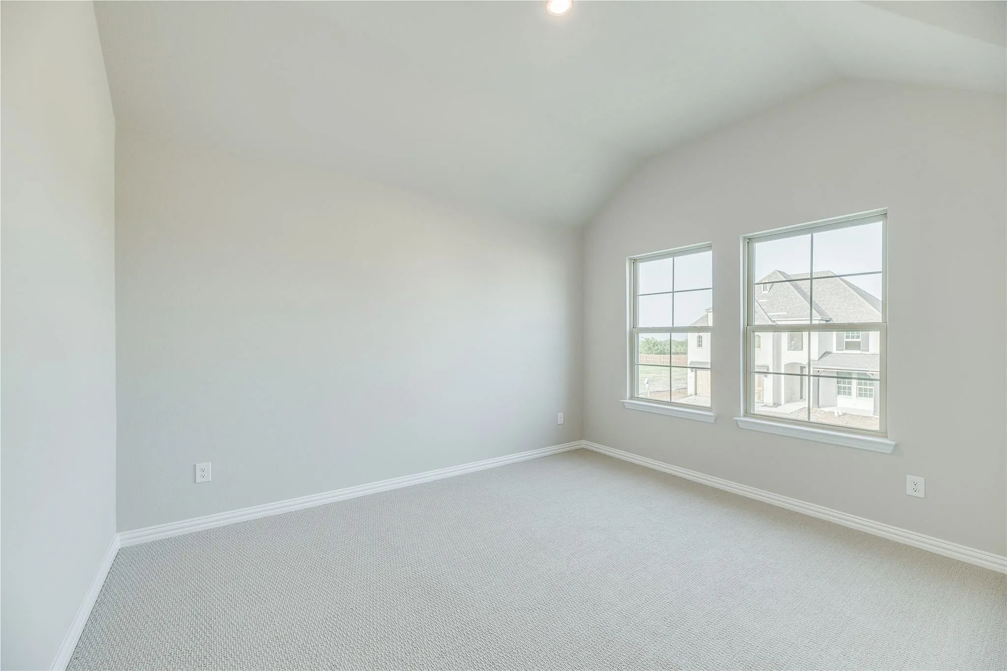 Vaulted ceiling with recessed lighting, two double-hung windows, and neutral carpeting