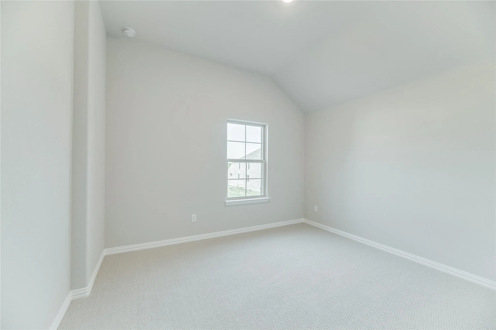 Vaulted ceiling, neutral wall paint, light-toned carpeting, white trim, and a window with grilles