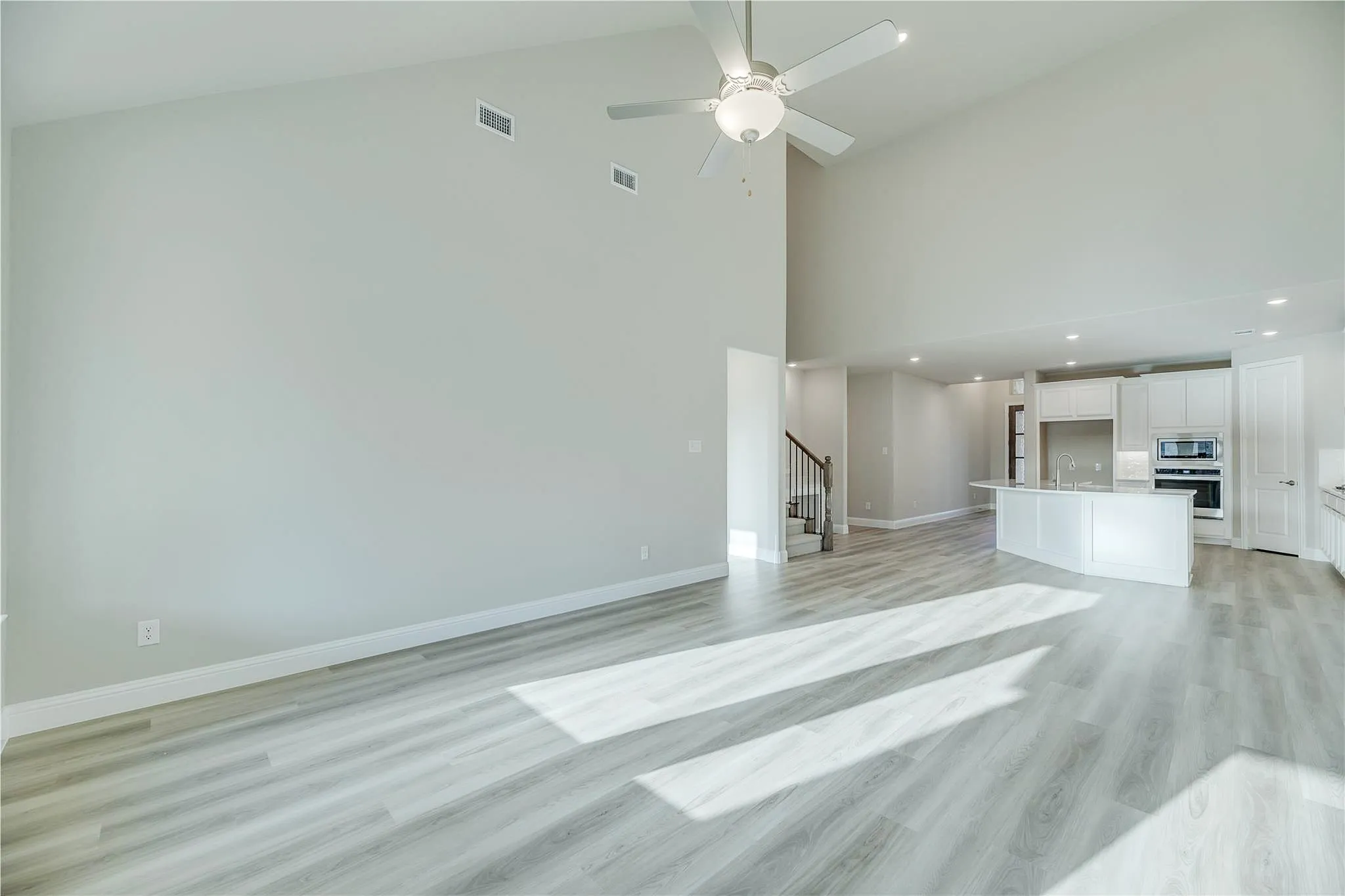 Vaulted ceilings with ceiling fan, wood-finish flooring, staircase with metal railings, white cabinetry, and recessed lighting