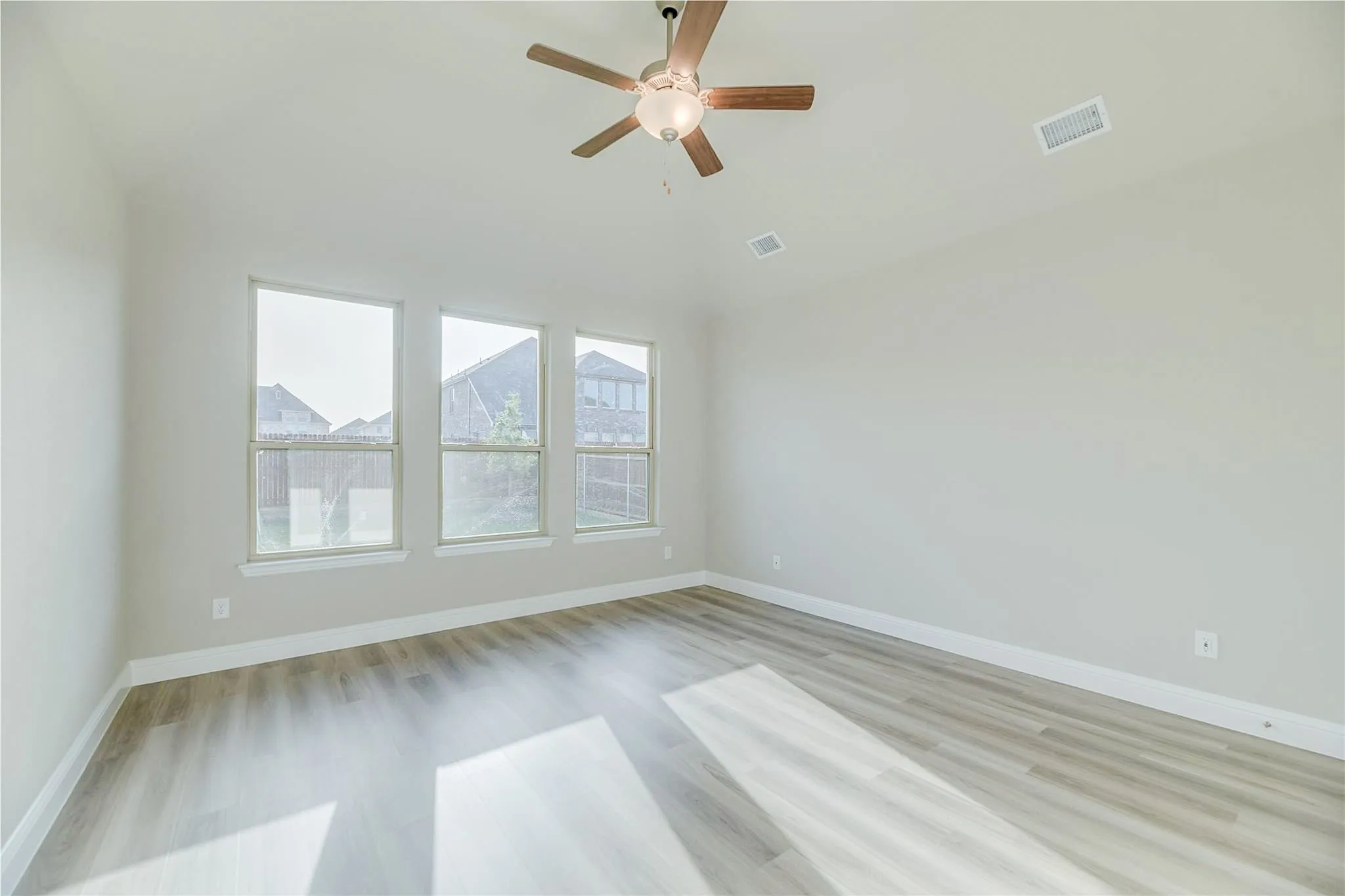 Light wood-finish flooring, three large windows, white trim, neutral wall tones, and a ceiling fan with integrated lighting