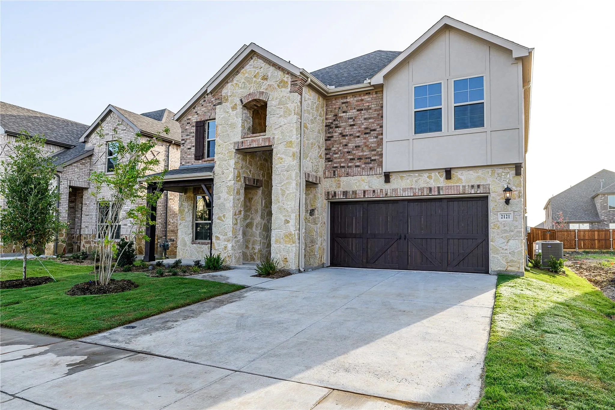 Stone and brick exterior with a covered entry, decorative garage door, and well-maintained lawn