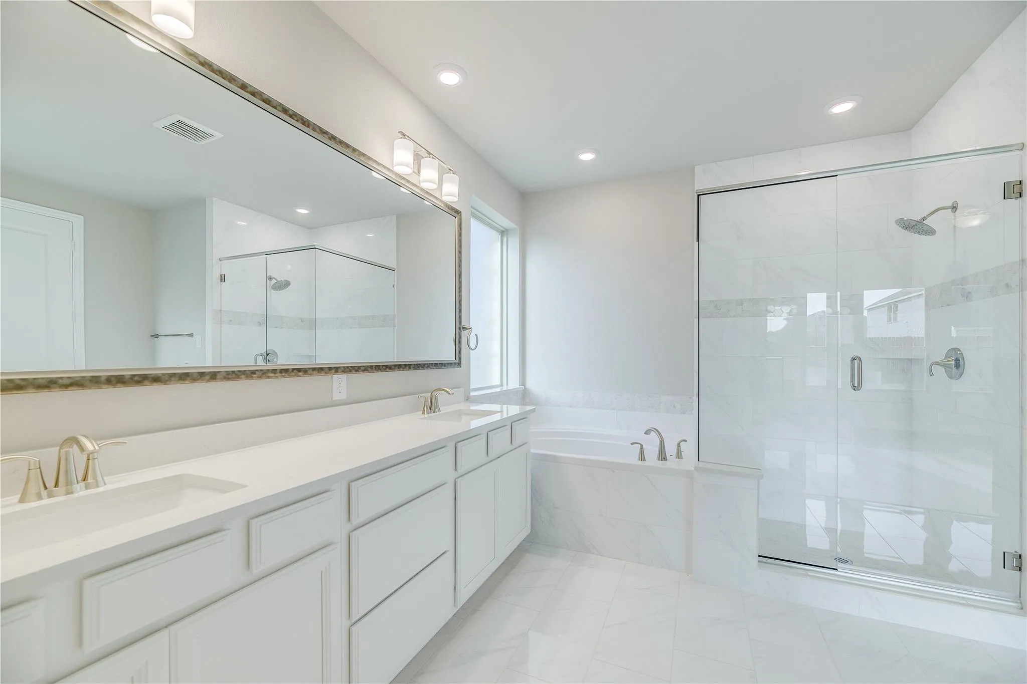 Dual vanity with undermount sinks and light-toned countertops, expansive wall-mounted mirror, built-in bathtub with tile surround, glass-enclosed shower with tile walls, and recessed lighting