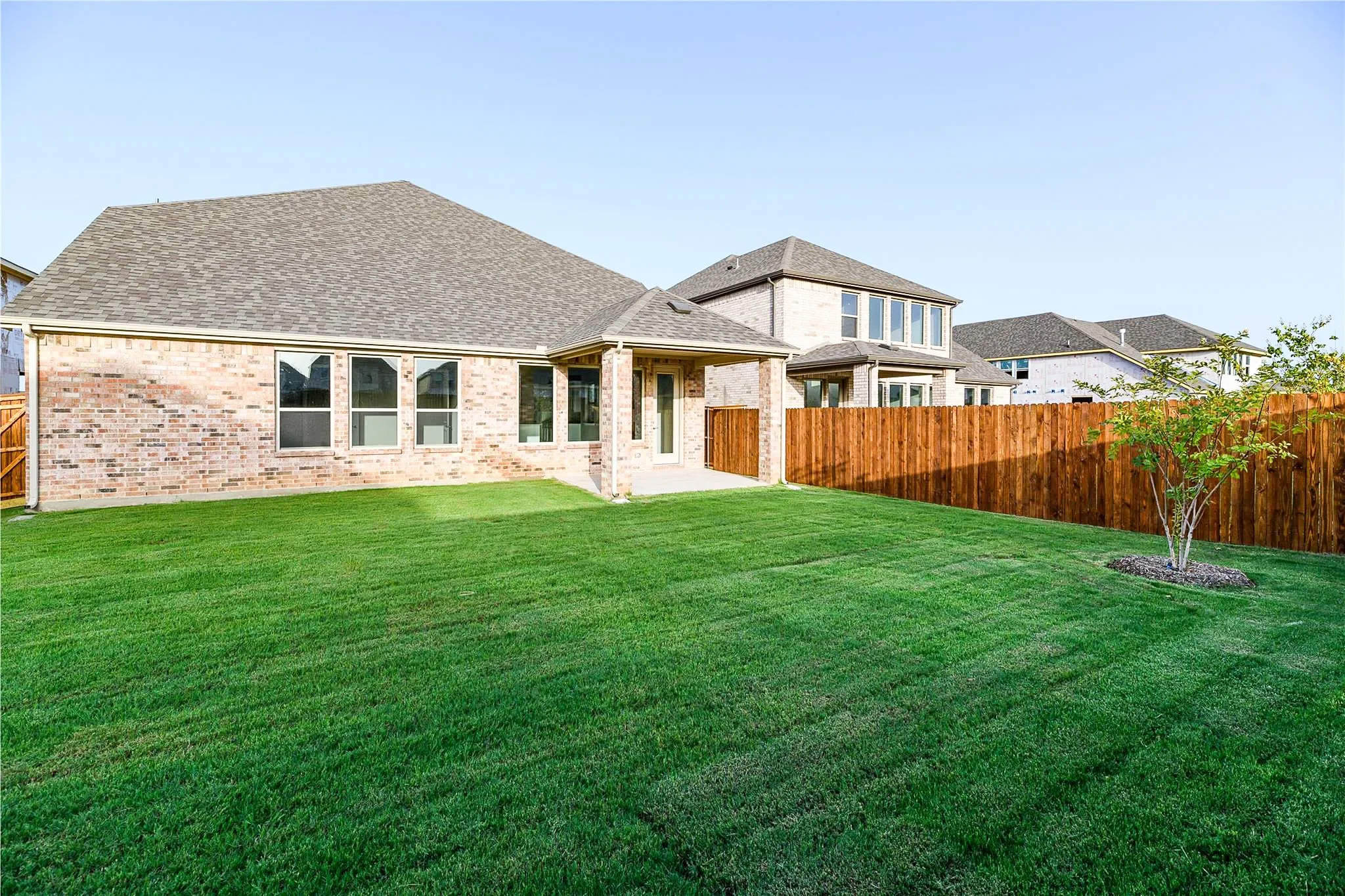 Expansive green lawn with a newly installed wood privacy fence, featuring a covered patio and multiple large windows along the brick exterior