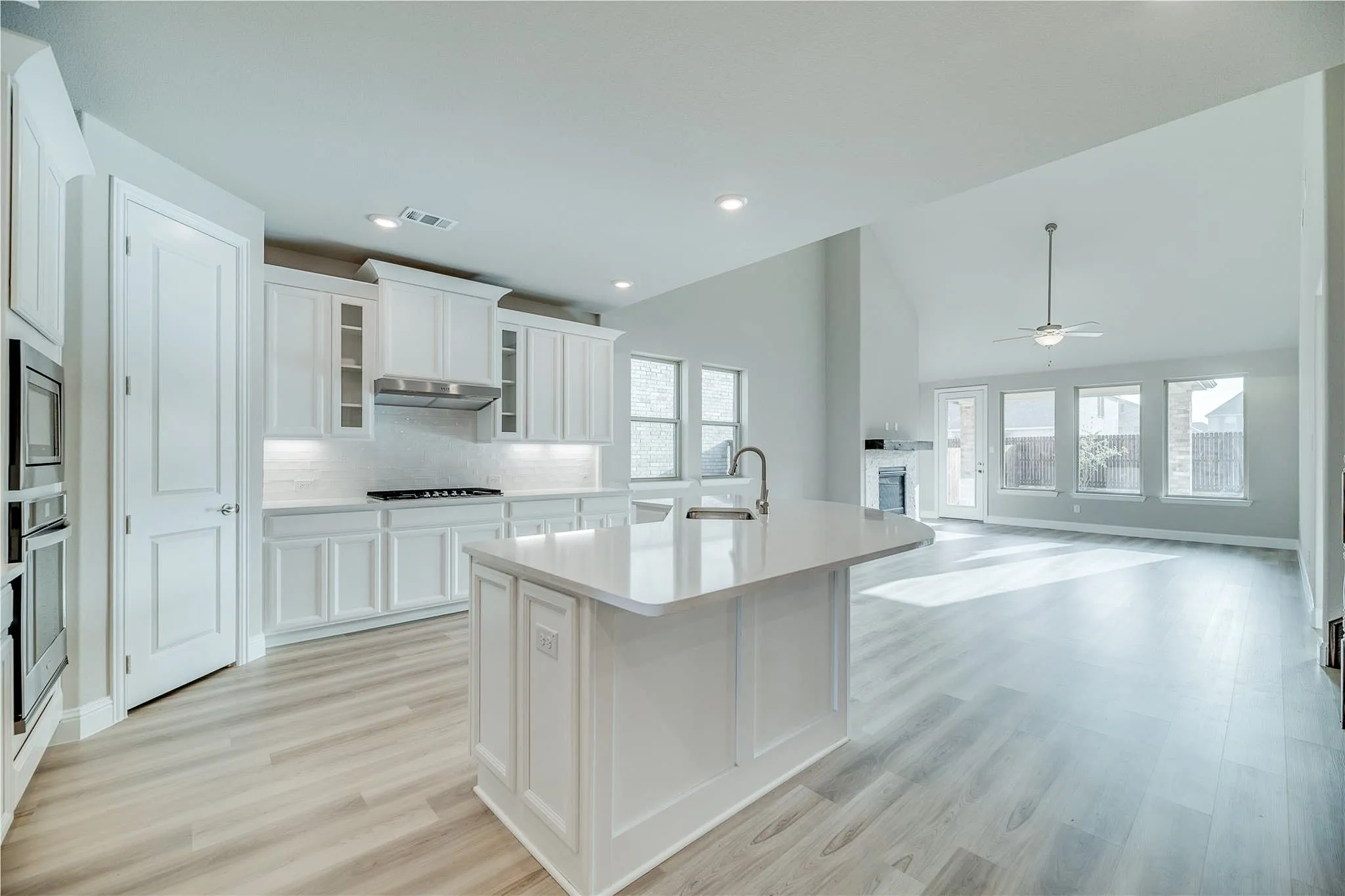 Kitchen featuring white cabinetry, built-in double ovens, a center island with a sink, and light wood-finish flooring
