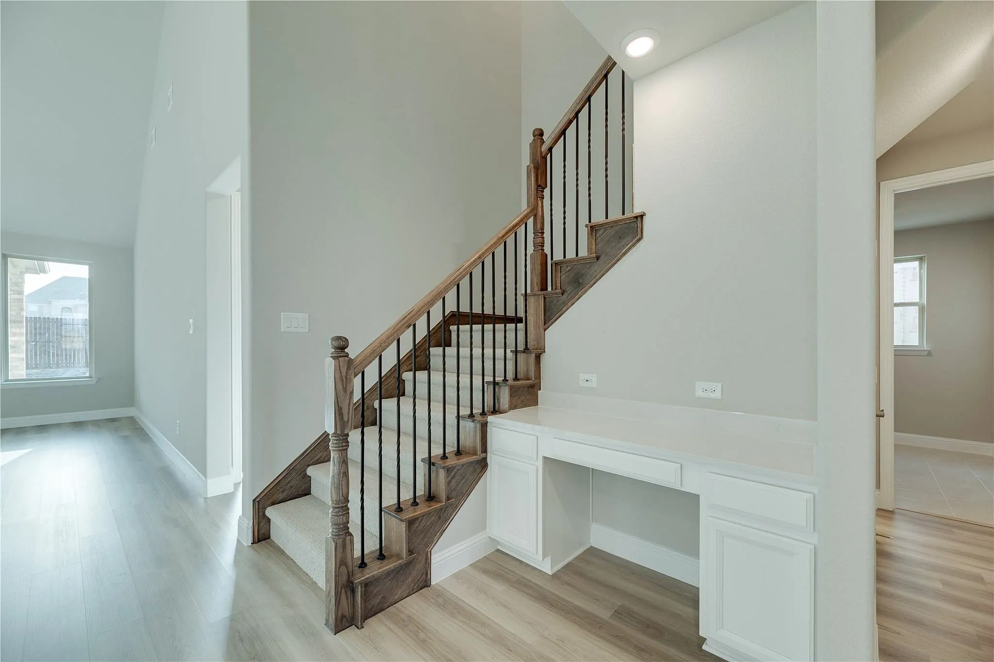 Hardwood-finish flooring, custom staircase with wrought iron balusters, built-in desk with white cabinetry, recessed lighting, and vaulted ceiling