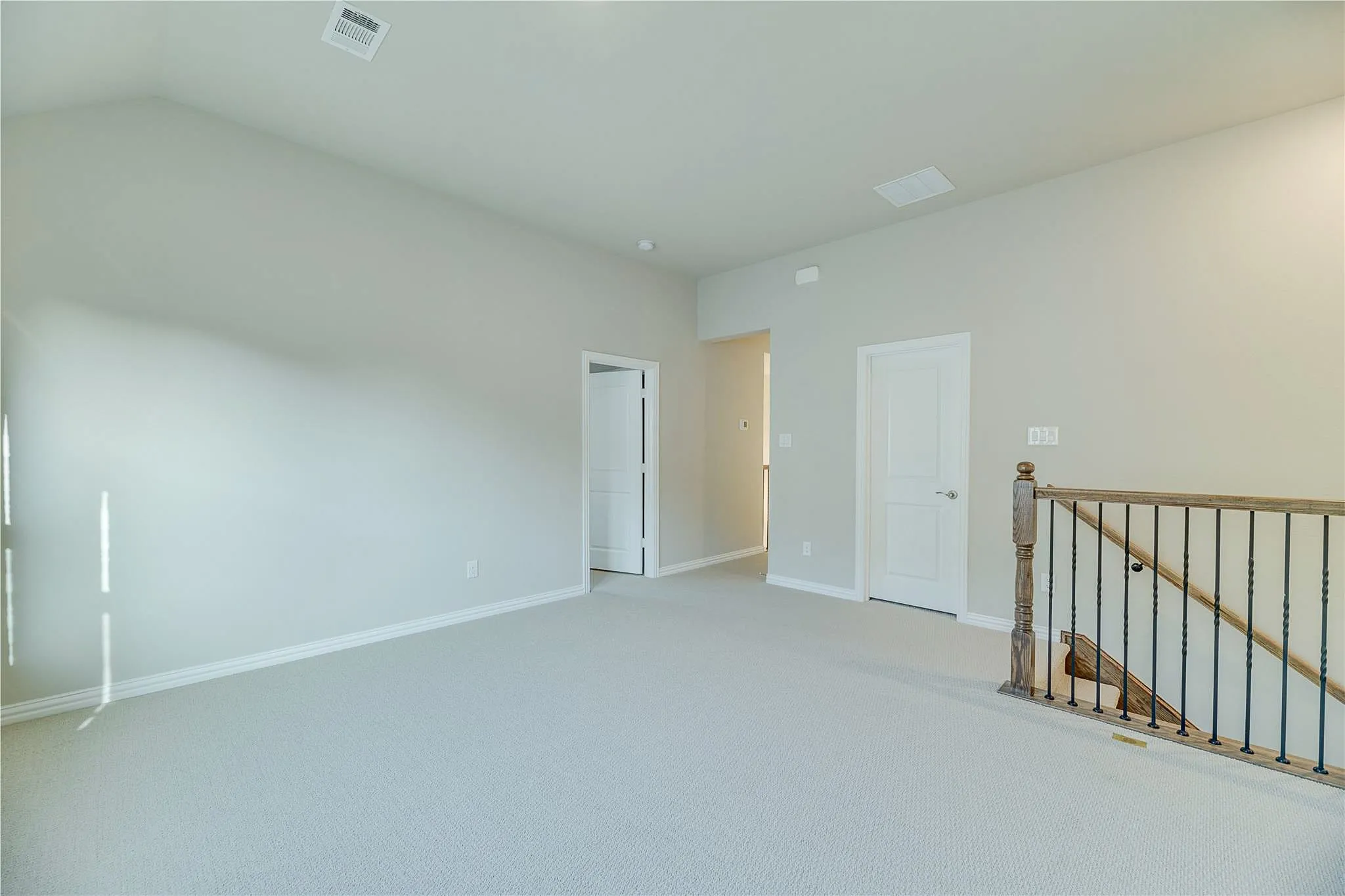 Vaulted ceiling, neutral wall paint, light-toned carpet, white paneled doors, and a wood and iron baluster railing