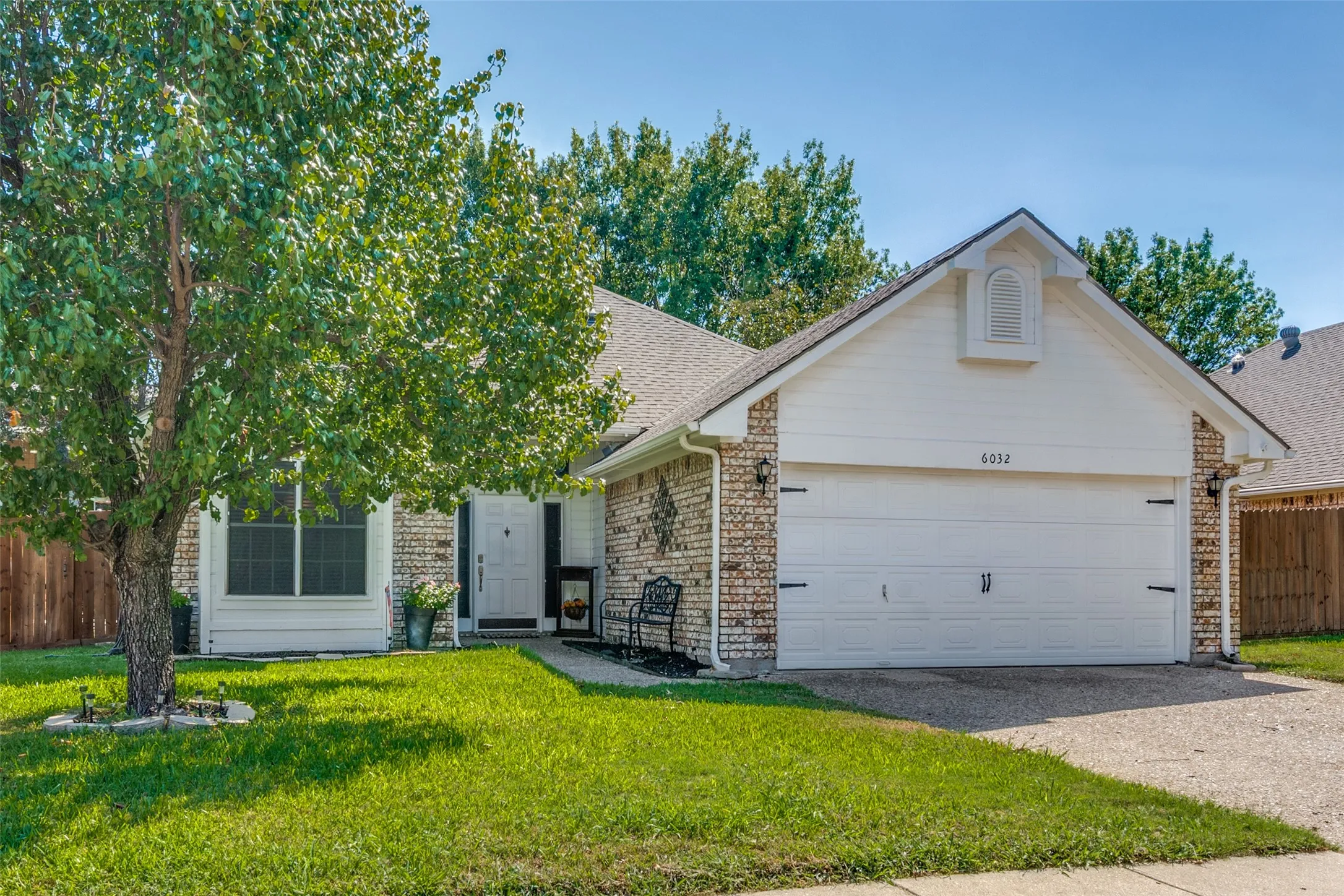 Brick and siding exterior with an attached two-car garage, mature front yard tree, and concrete driveway