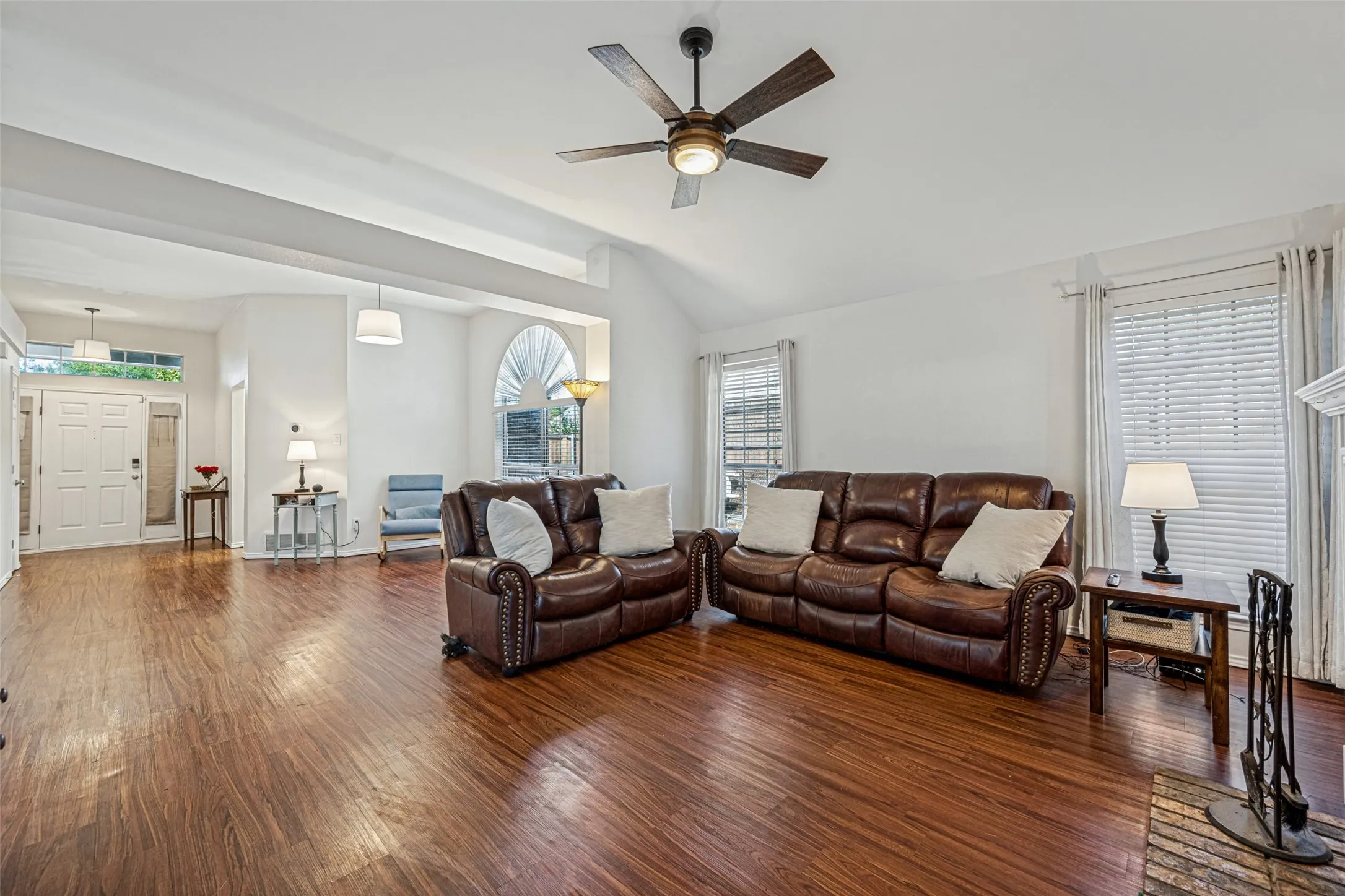 Vaulted ceiling with a ceiling fan, wood-finish flooring, multiple windows, and a white front entry door with transom window