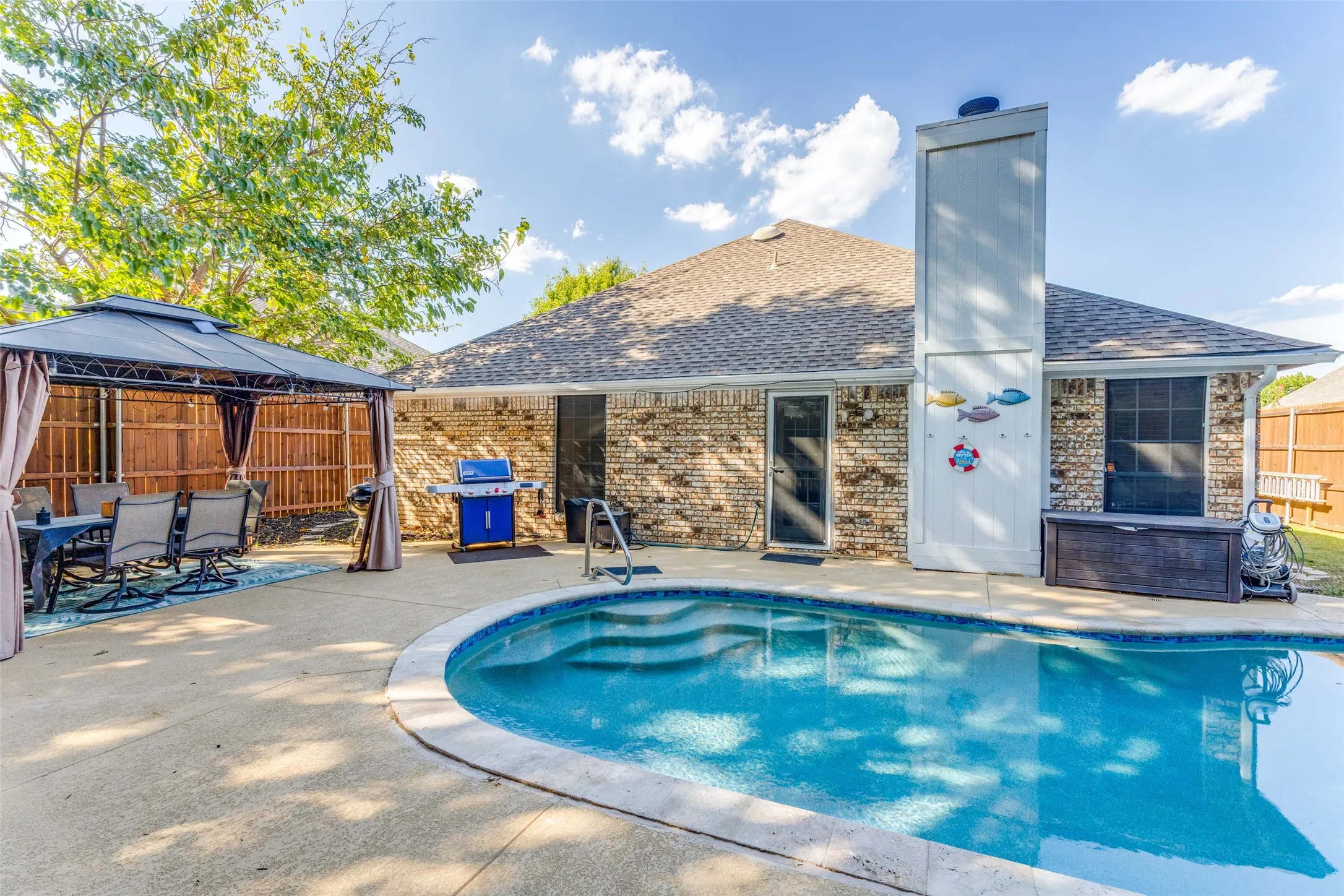 Brick exterior with a peaked roofline, featuring a swimming pool with integrated steps, and a concrete patio