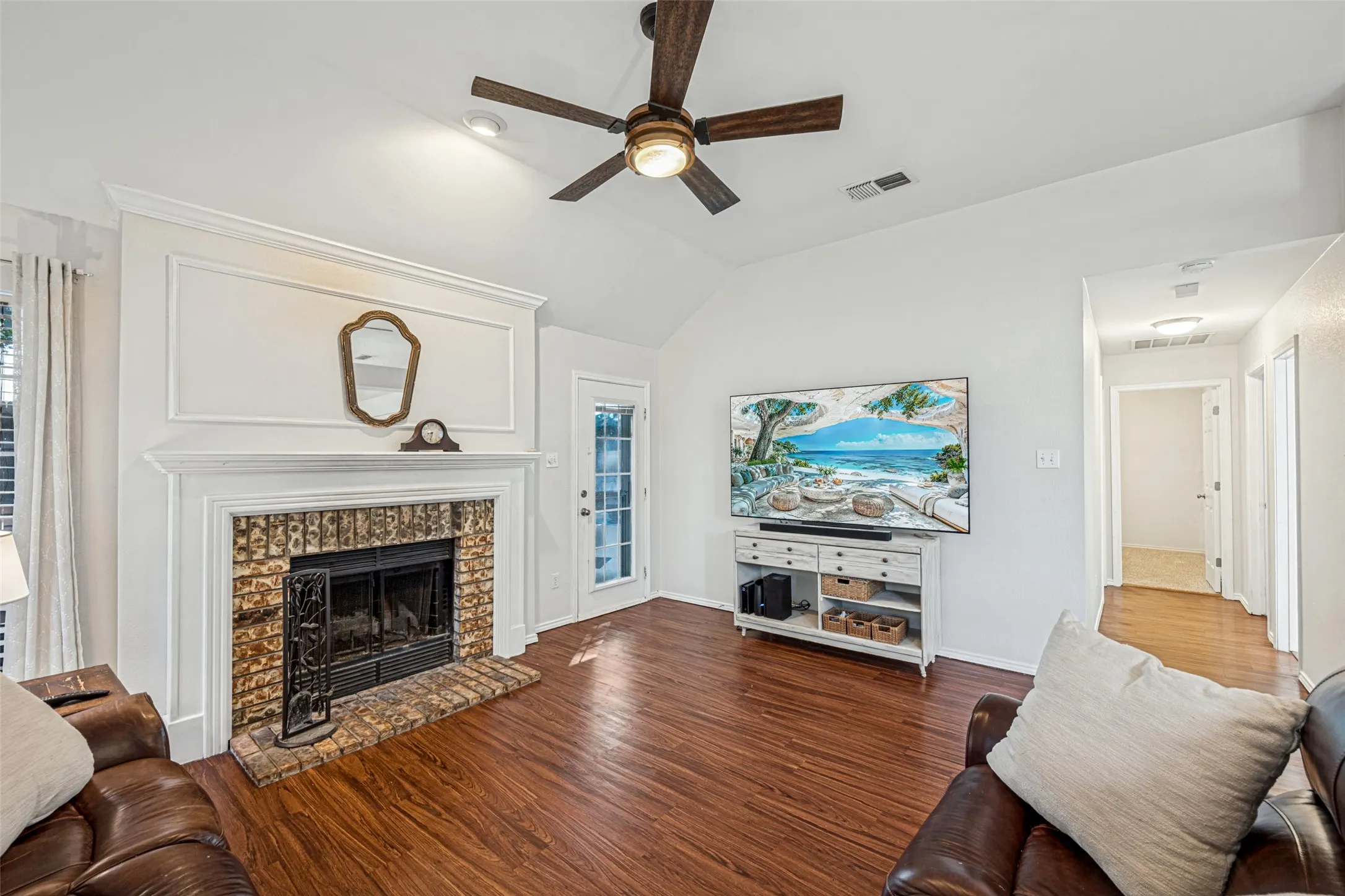 Vaulted ceilings, wood-finish flooring, and a brick fireplace with a detailed white mantel