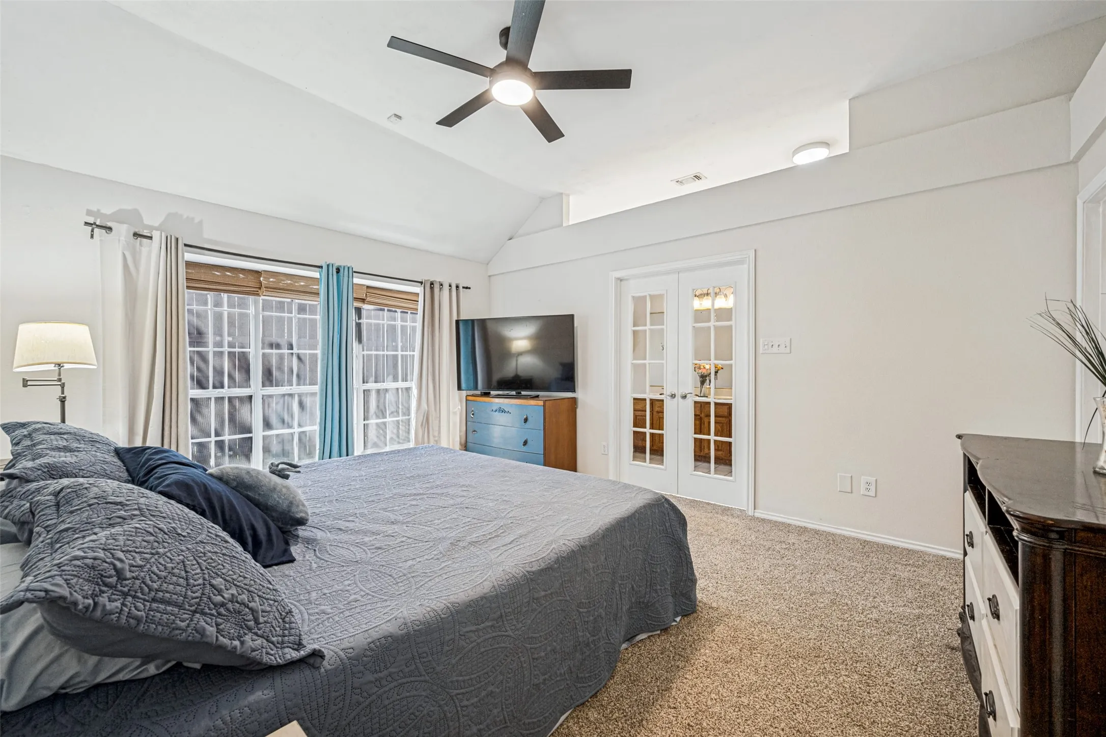 Vaulted ceiling, ceiling fan, large windows, French doors with glass panes, and textured carpeting