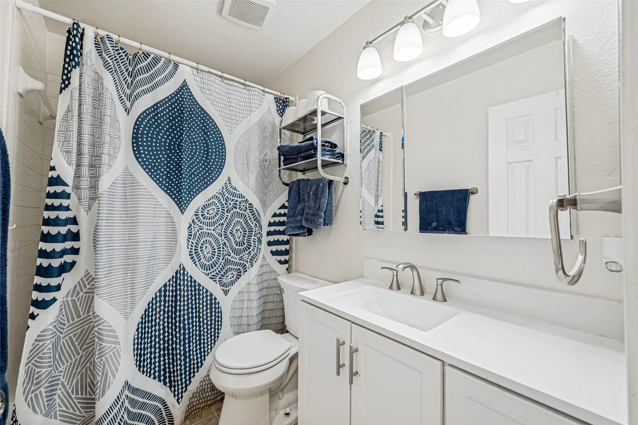 Bathroom featuring a white vanity with an integrated sink, brushed nickel faucet, large wall-mounted mirror, and overhead track lighting with three sconces