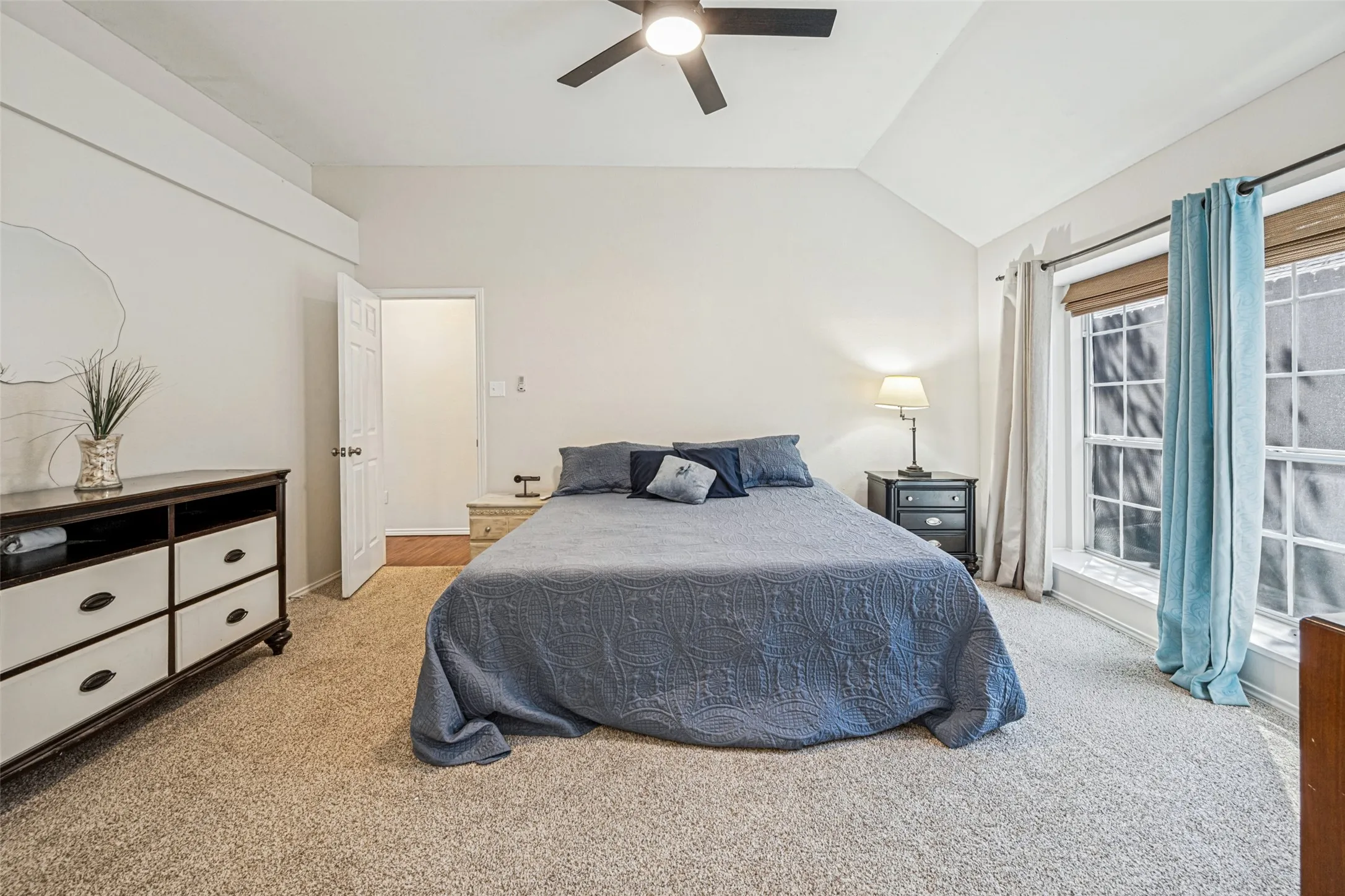 Vaulted ceiling with an integrated ceiling fan, light-toned carpet flooring, and a large window with blinds