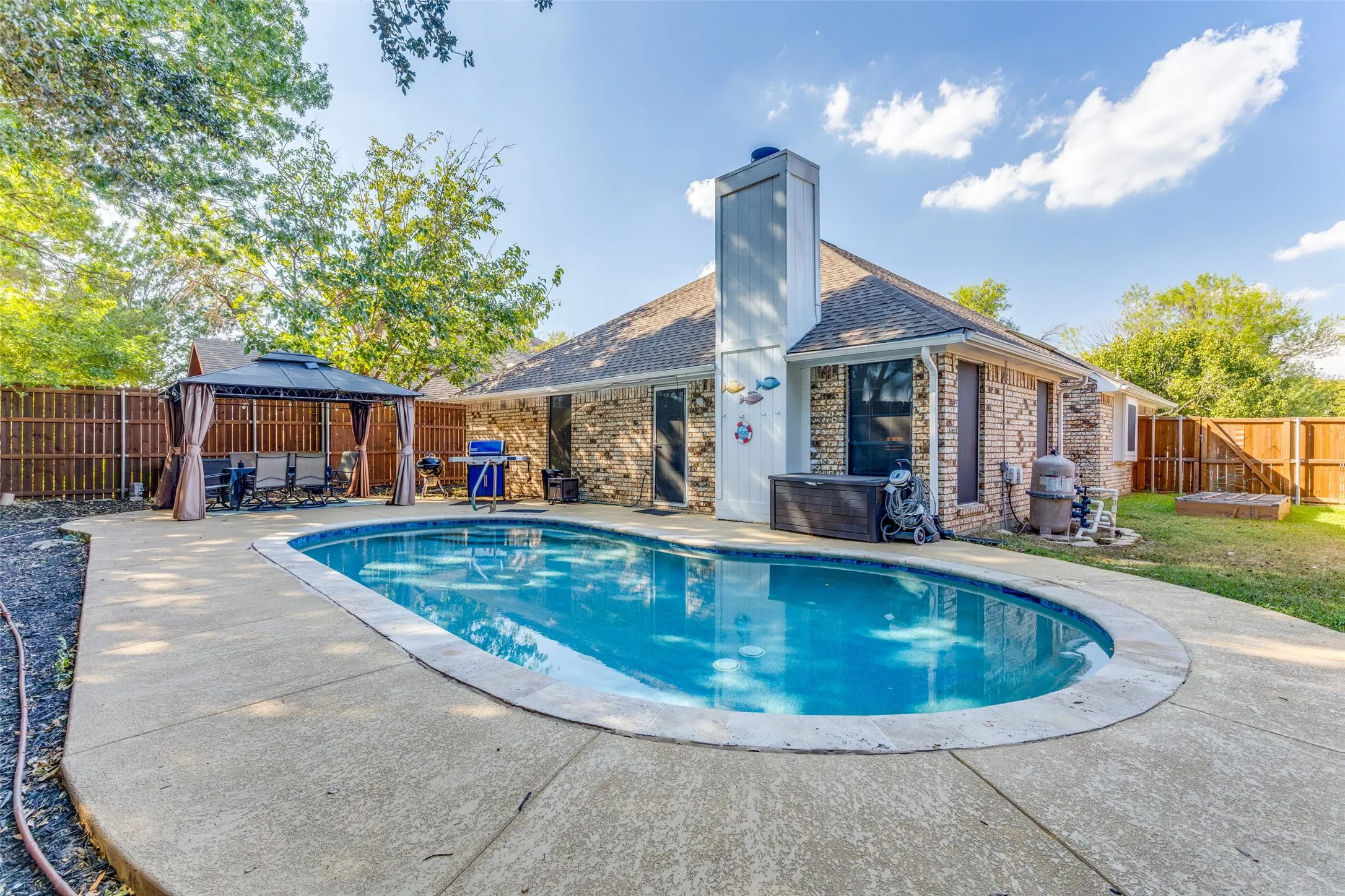 In-ground swimming pool with surrounding concrete patio, brick exterior, and a privacy fence