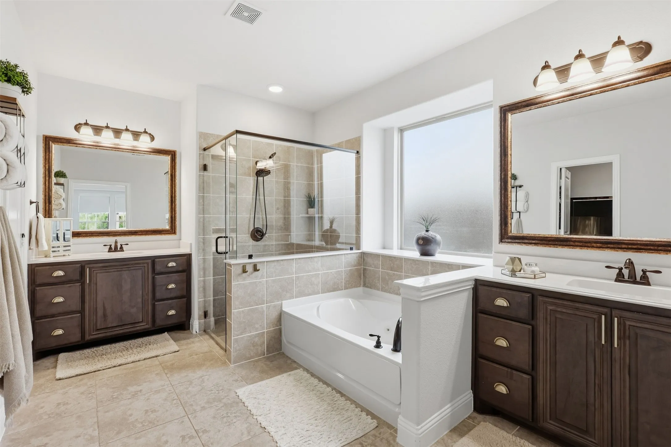 Primary ensuite bathroom with dual vanities with integrated sinks, framed mirrors, a glass-enclosed shower, a built-in soaking tub, water closet and large walk in closet