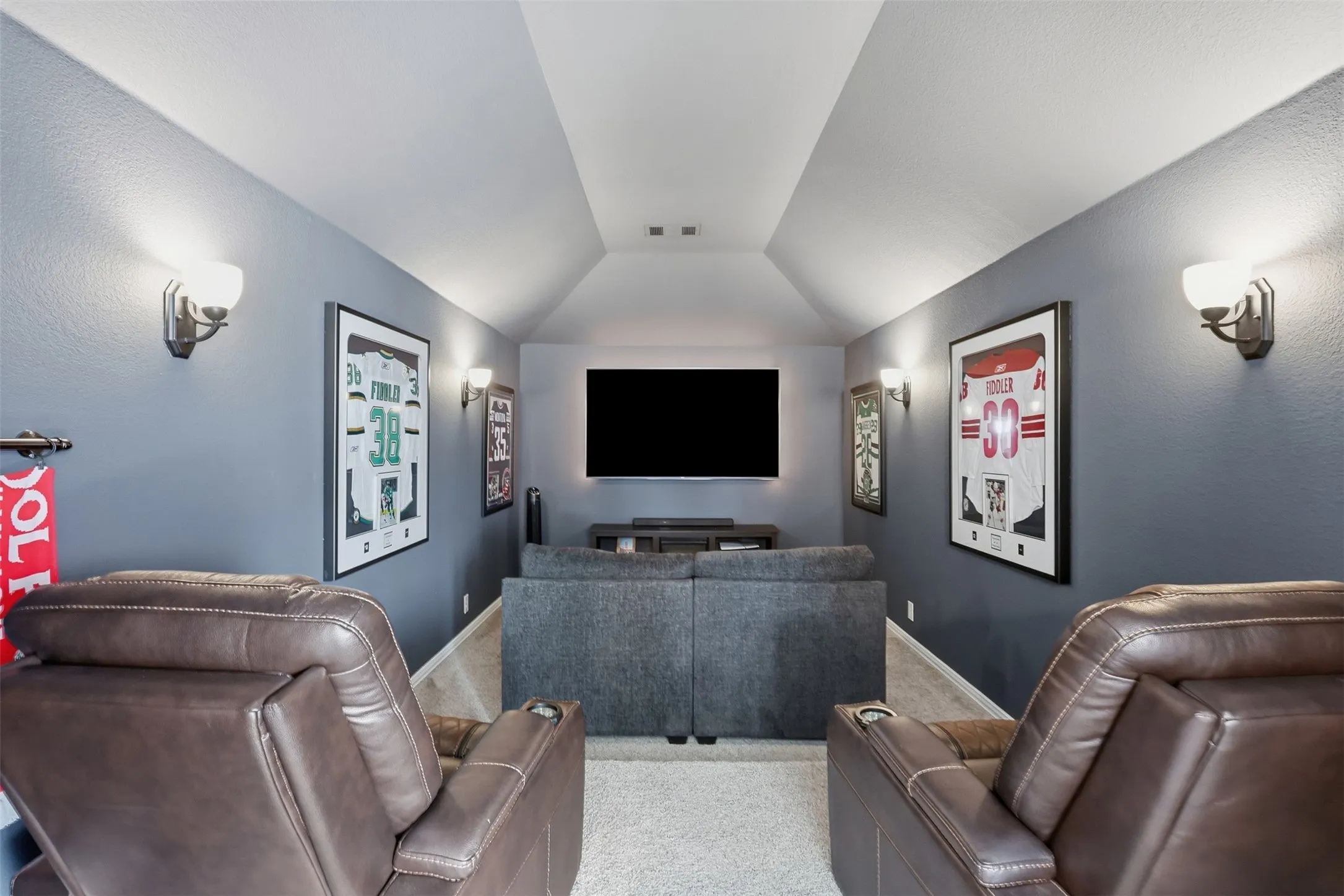 Upstairs media room with vaulted ceiling, recessed lighting, wall-mounted sconces, and carpeting throughout.