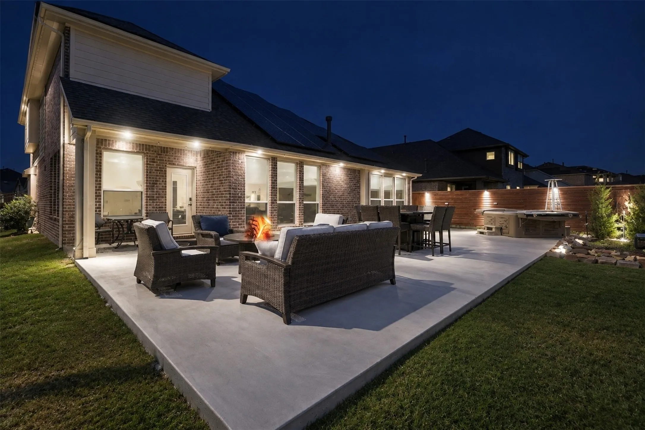 Expansive concrete patio with integrated fire pit, built-in spa, brick exterior, and wood fencing