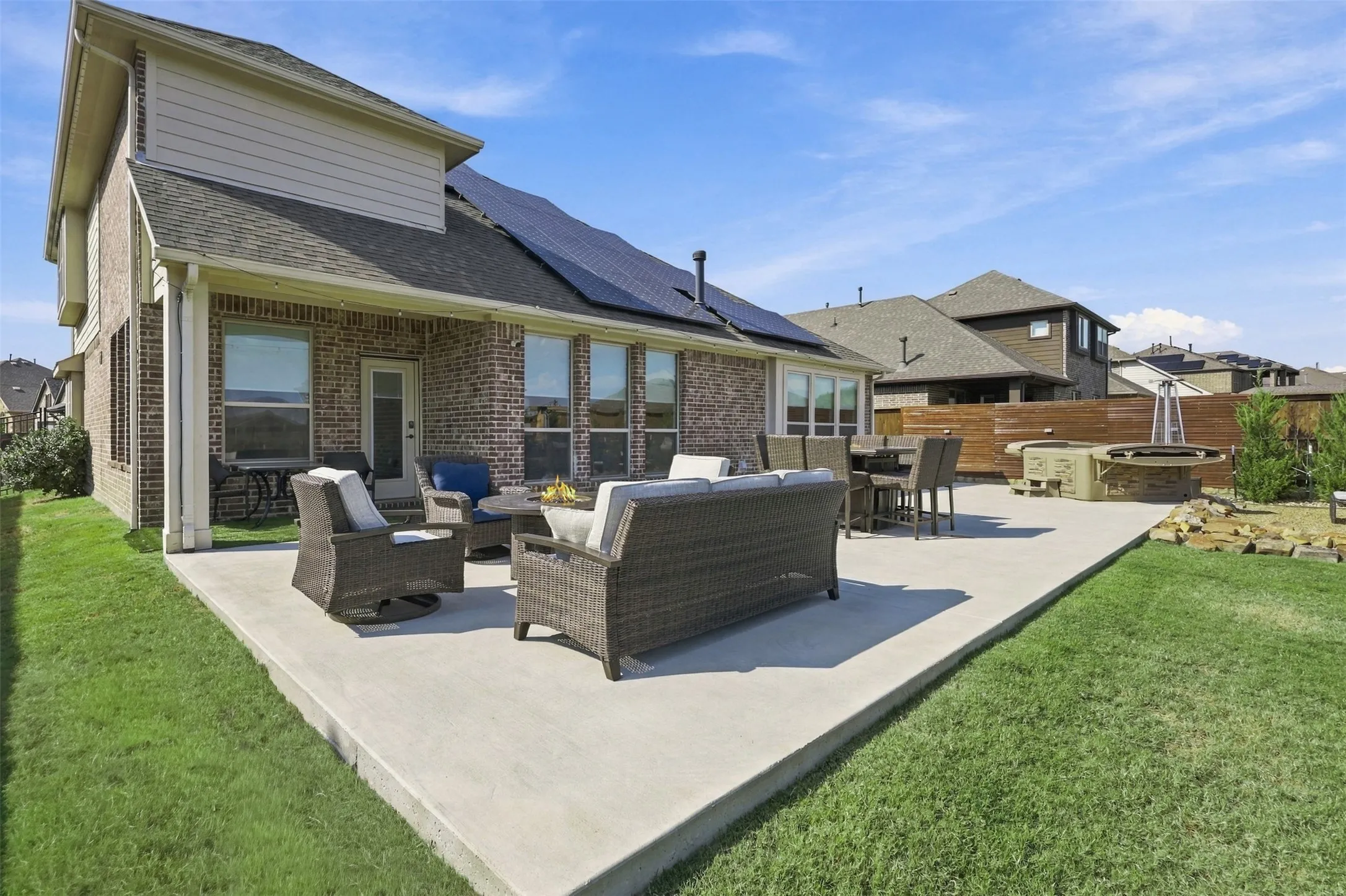 Expansive concrete patio with a covered outdoor area, brick exterior, and a built-in fire pit
