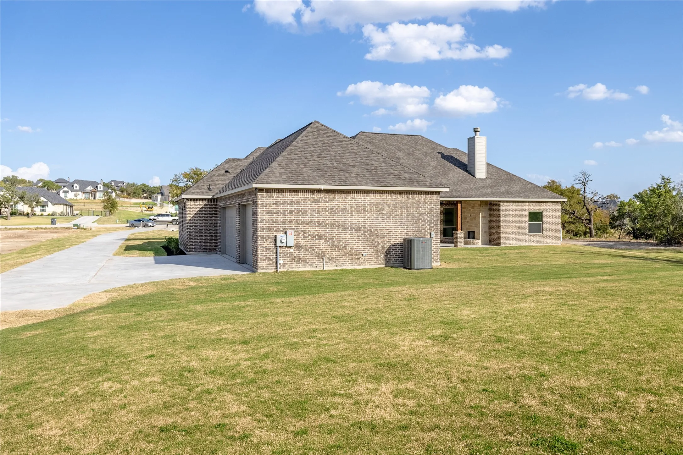Brick exterior with an attached garage, paved driveway, and covered patio