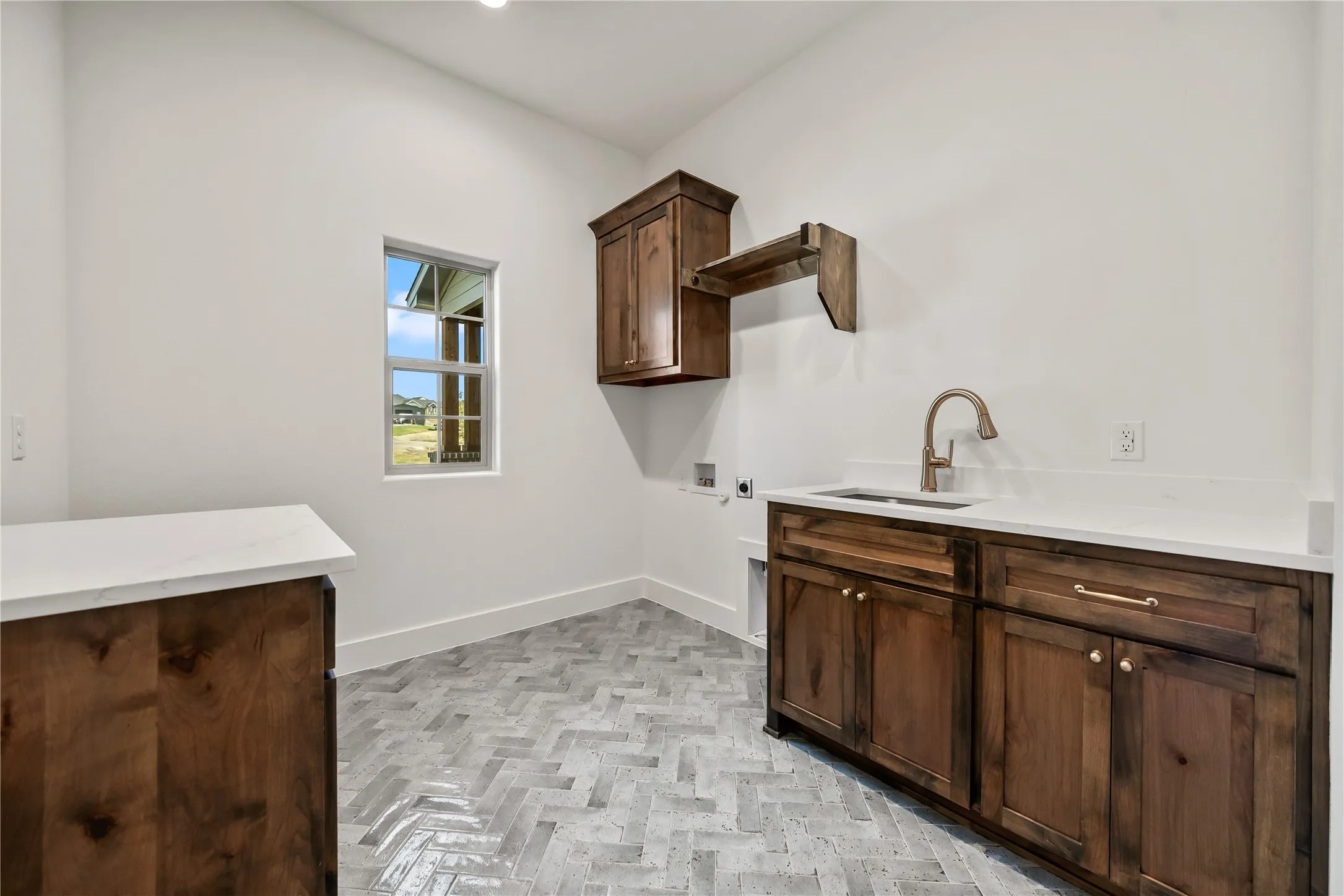 Herringbone-patterned floor tiling, wood-finish cabinetry, built-in sink, and white countertops