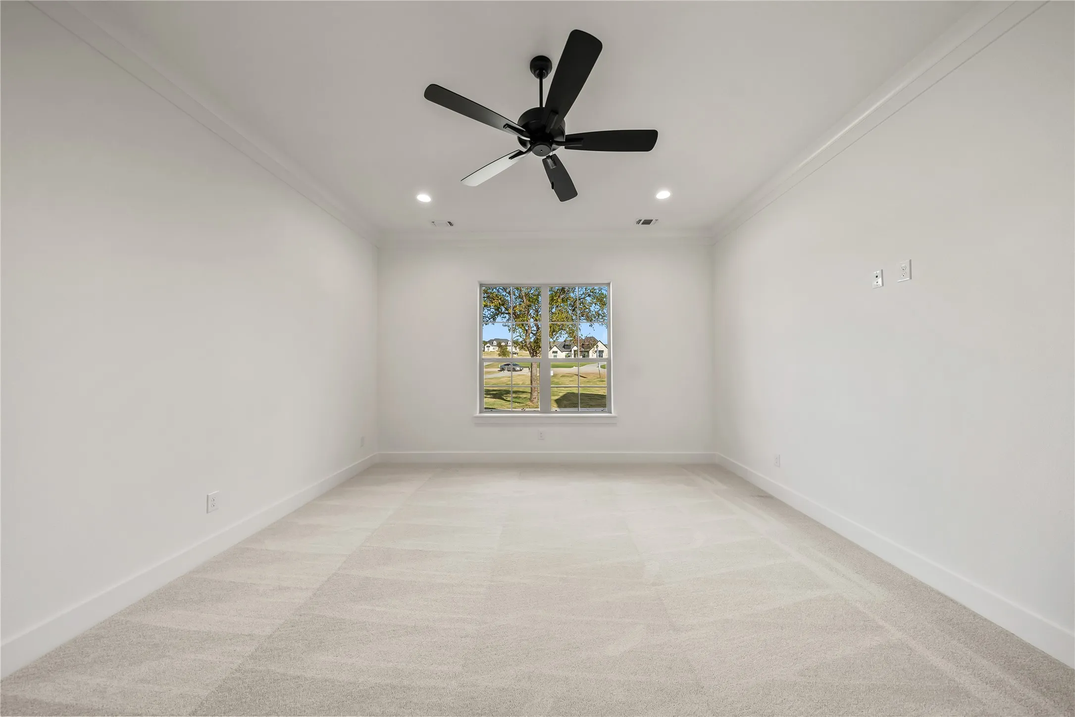 Recessed lighting, crown molding, and a modern ceiling fan complement the neutral carpet flooring and large window