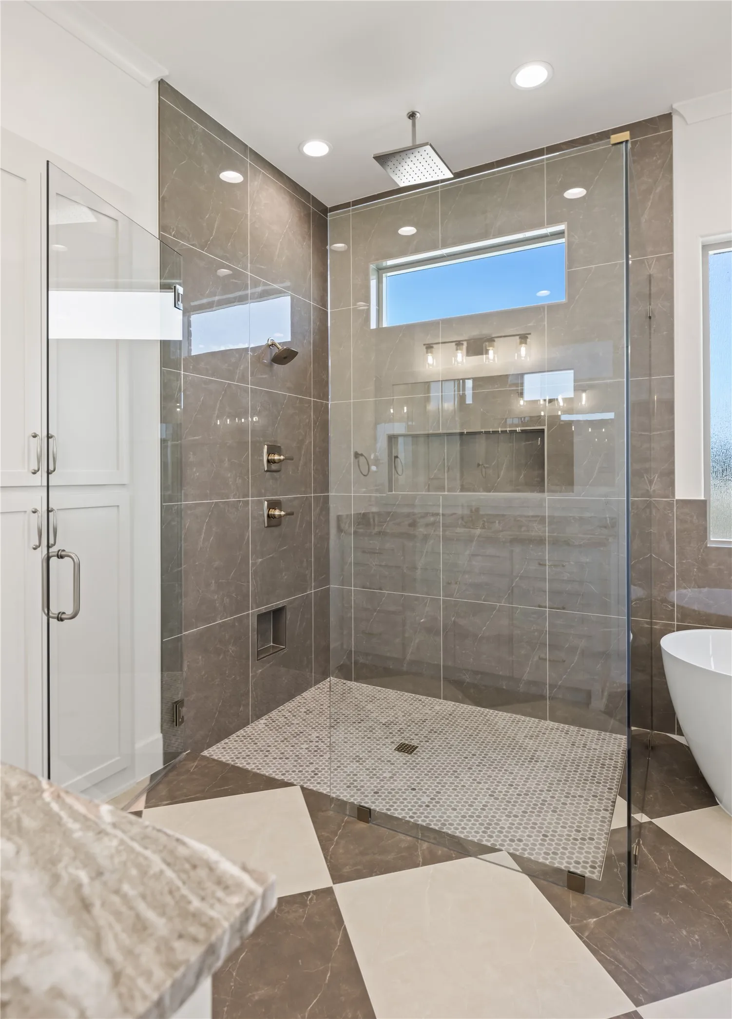 Glass-enclosed shower with large format tile walls, mosaic tile floor, and a rainfall showerhead