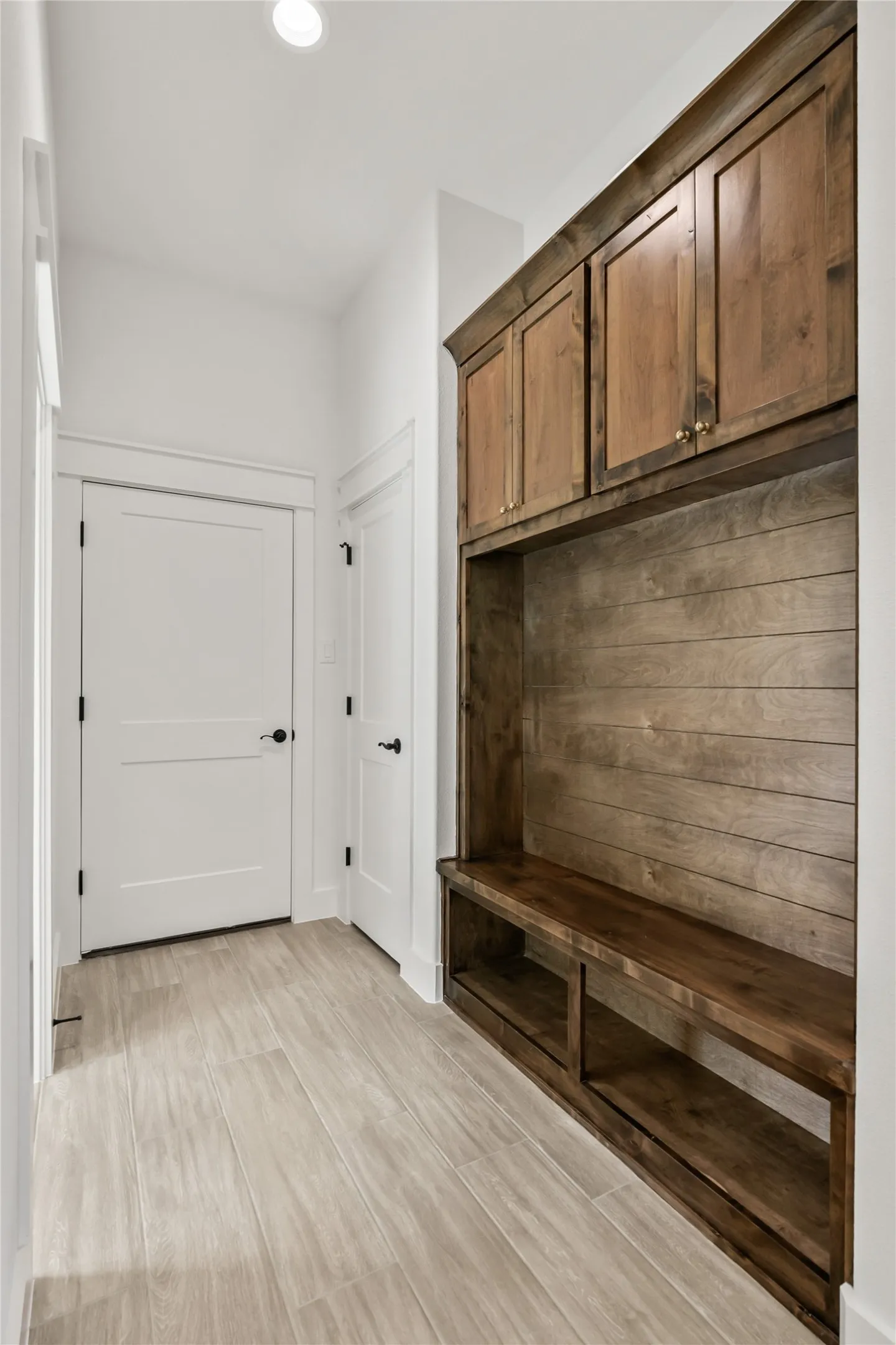 Built-in wooden bench with storage cubbies and upper cabinetry, complemented by light wood-finish flooring and white interior doors