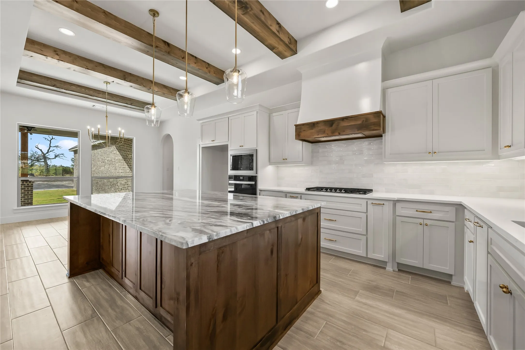 Spacious kitchen featuring a large island with a substantial countertop, white cabinetry, integrated stainless steel appliances, and wood-finish ceiling beams