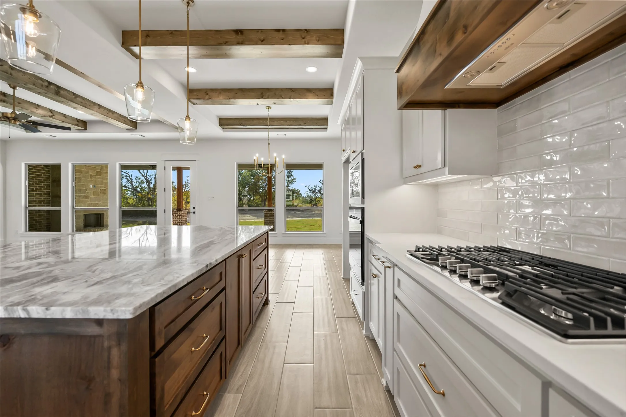 Gourmet kitchen featuring a gas range, white subway tile backsplash, white cabinetry, dark wood island with light stone countertop, and exposed wood ceiling beams