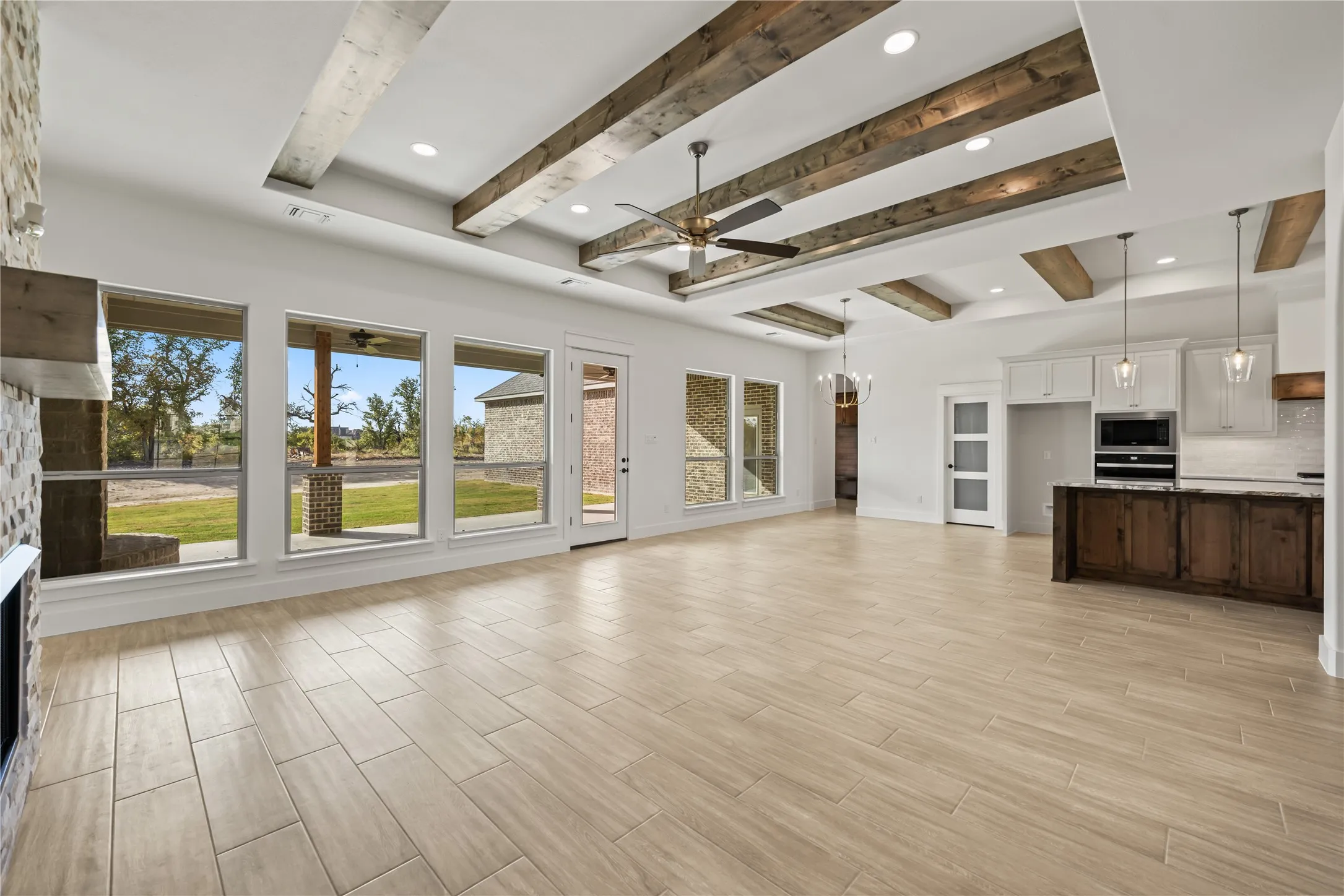 Tile flooring, coffered ceiling with exposed wood beams, stone-clad fireplace, integrated kitchen with island, and large windows with outdoor access