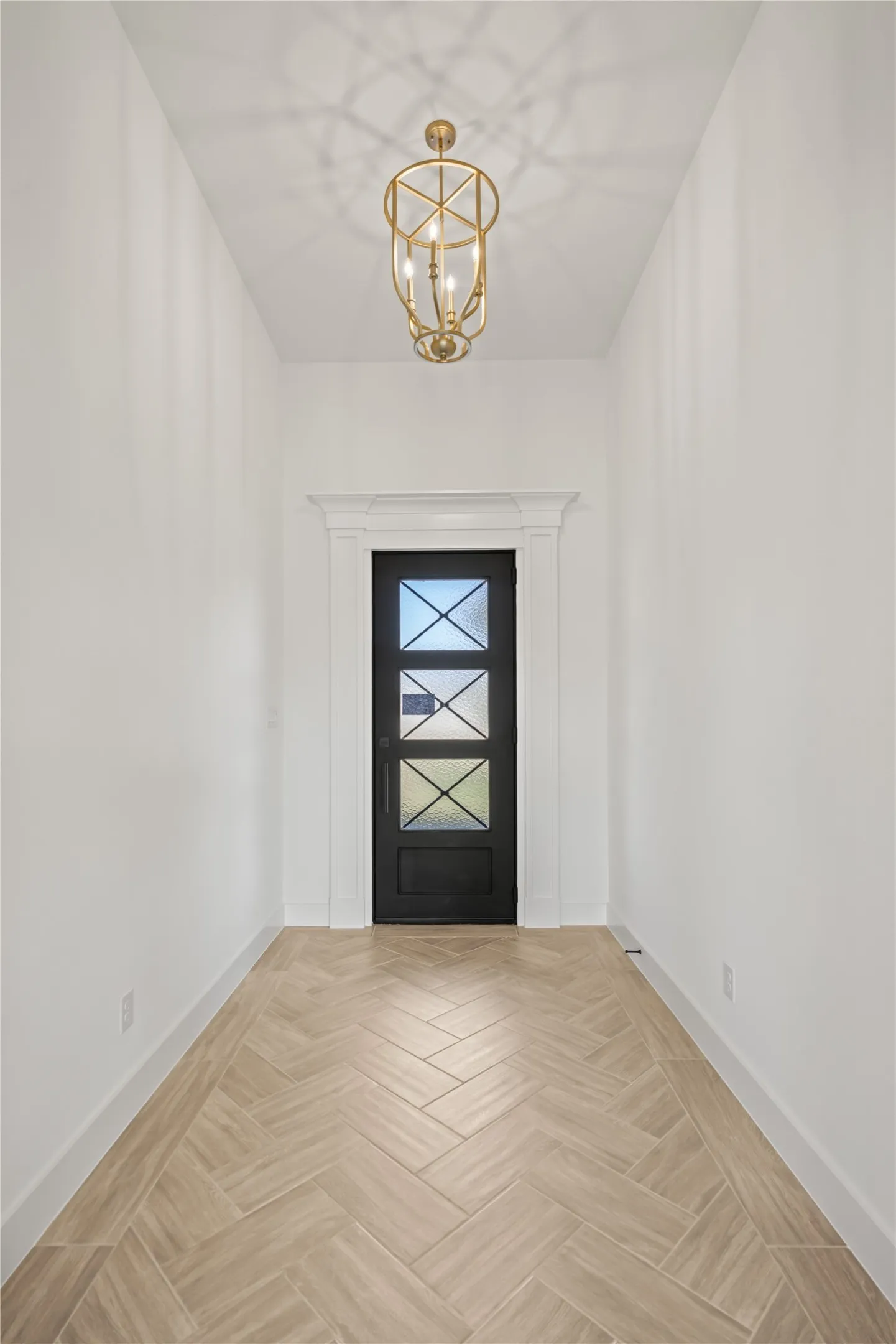 Herringbone-patterned wood-finish flooring, a decorative three-light chandelier, and a black paneled door with frosted glass inserts