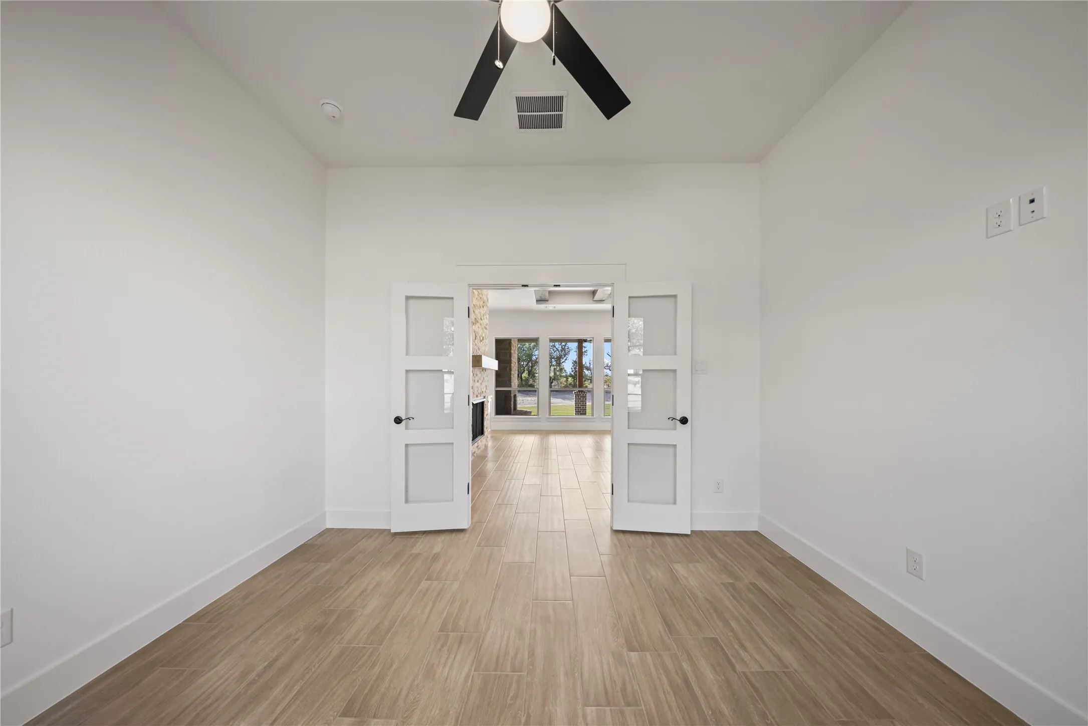 Room featuring wood-finish tile flooring, a ceiling fan with integrated lighting, and double French doors with frosted glass panels