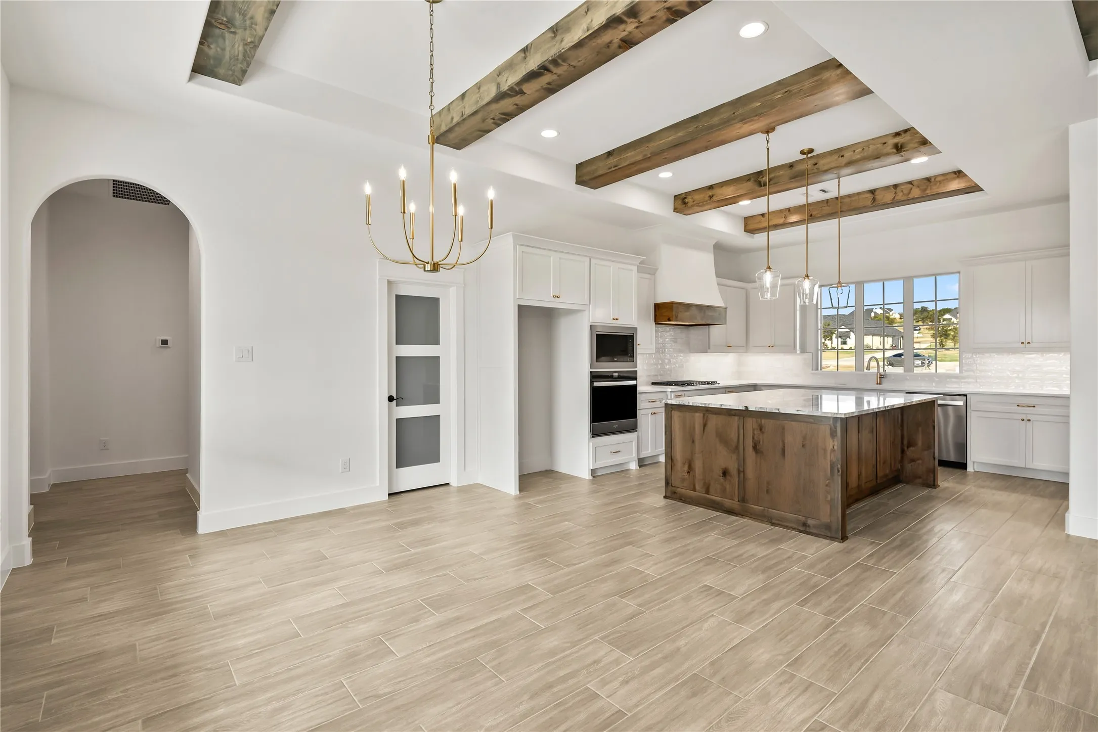Wood-finish flooring, exposed wood ceiling beams, kitchen island with built-in cabinetry, stainless steel appliances, and a polished chandelier