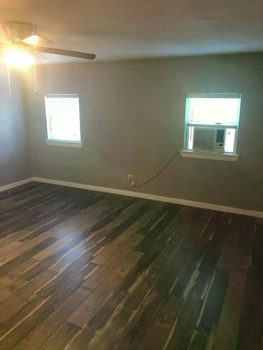 Wood-finish flooring, two windows with white trim, and a ceiling fan with integrated lighting