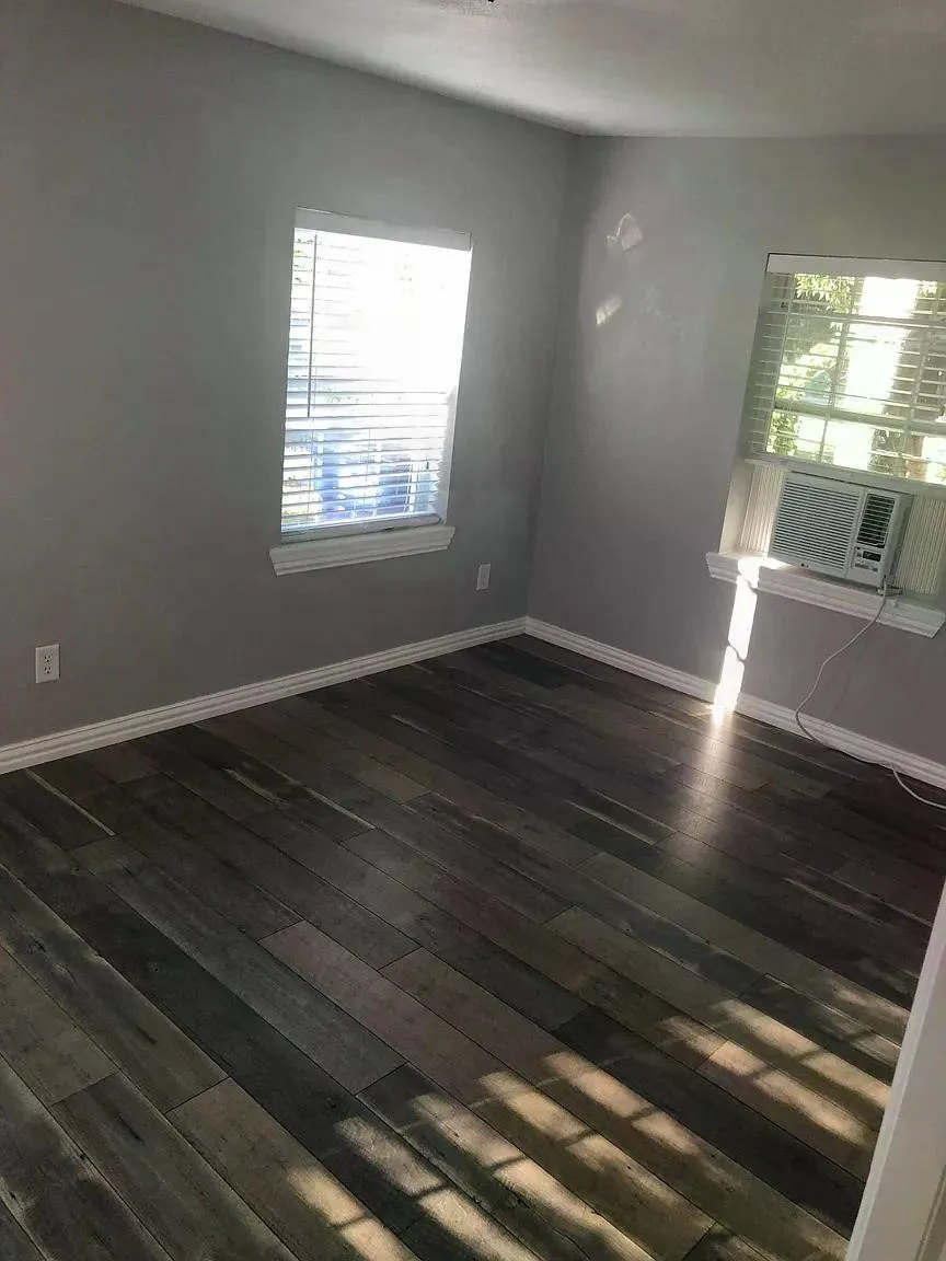 Wood-finish flooring with white baseboards, two windows with blinds, and light gray wall paint