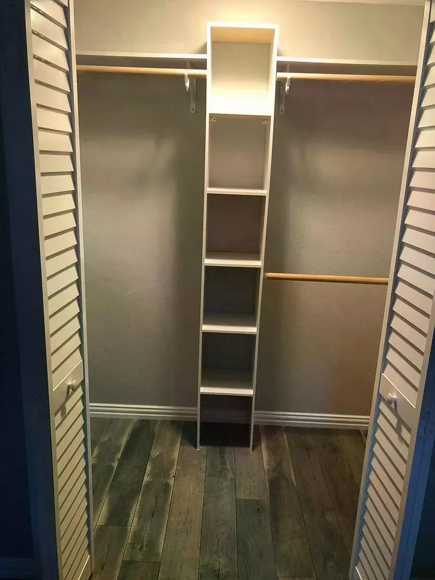 Louvered bifold doors opening to a closet featuring wood-finish flooring, built-in shelving, and dual hanging rods