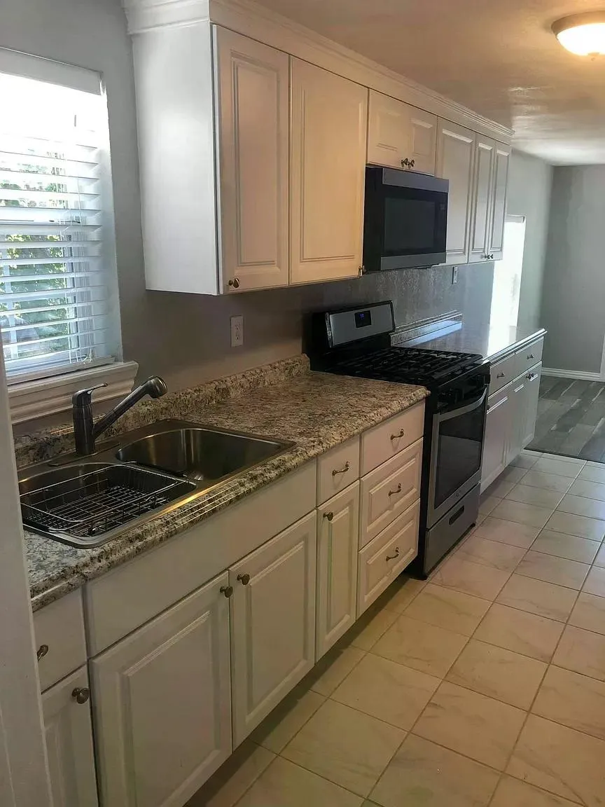 White shaker-style cabinetry with crown molding, granite-style countertops, stainless steel sink with high-arc faucet, and tiled flooring