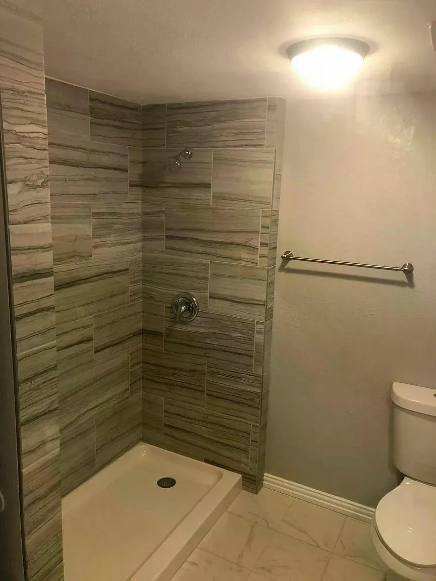 Tiled shower enclosure with a rainfall shower head, single-handle shower control, and a white shower pan