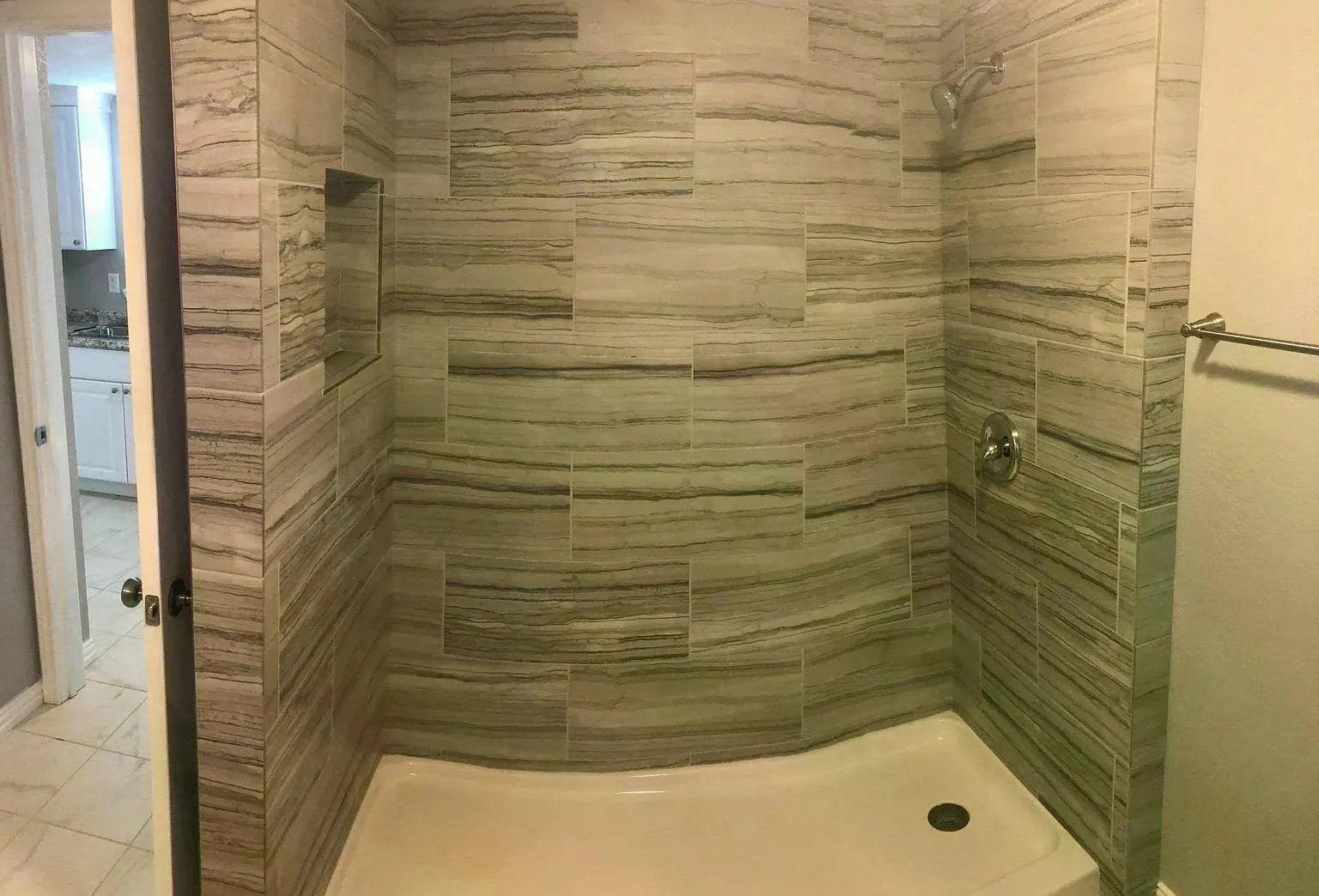 Tiled shower enclosure featuring a built-in niche, chrome showerhead, and coordinating fixture