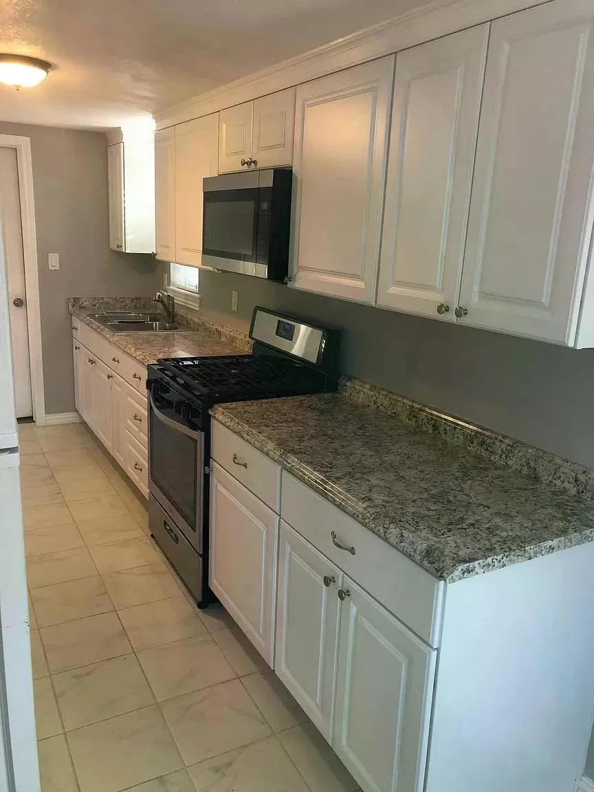 Crisp white cabinetry with crown molding, granite-finish countertops, stainless steel appliances, and tiled flooring