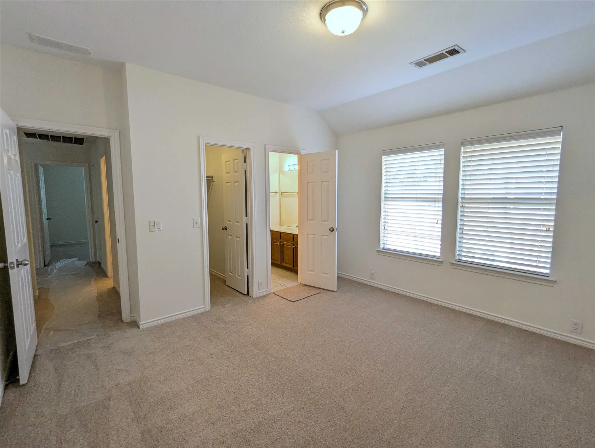 Carpeted flooring, vaulted ceiling, two windows with blinds, flush mount ceiling light, and panel doors