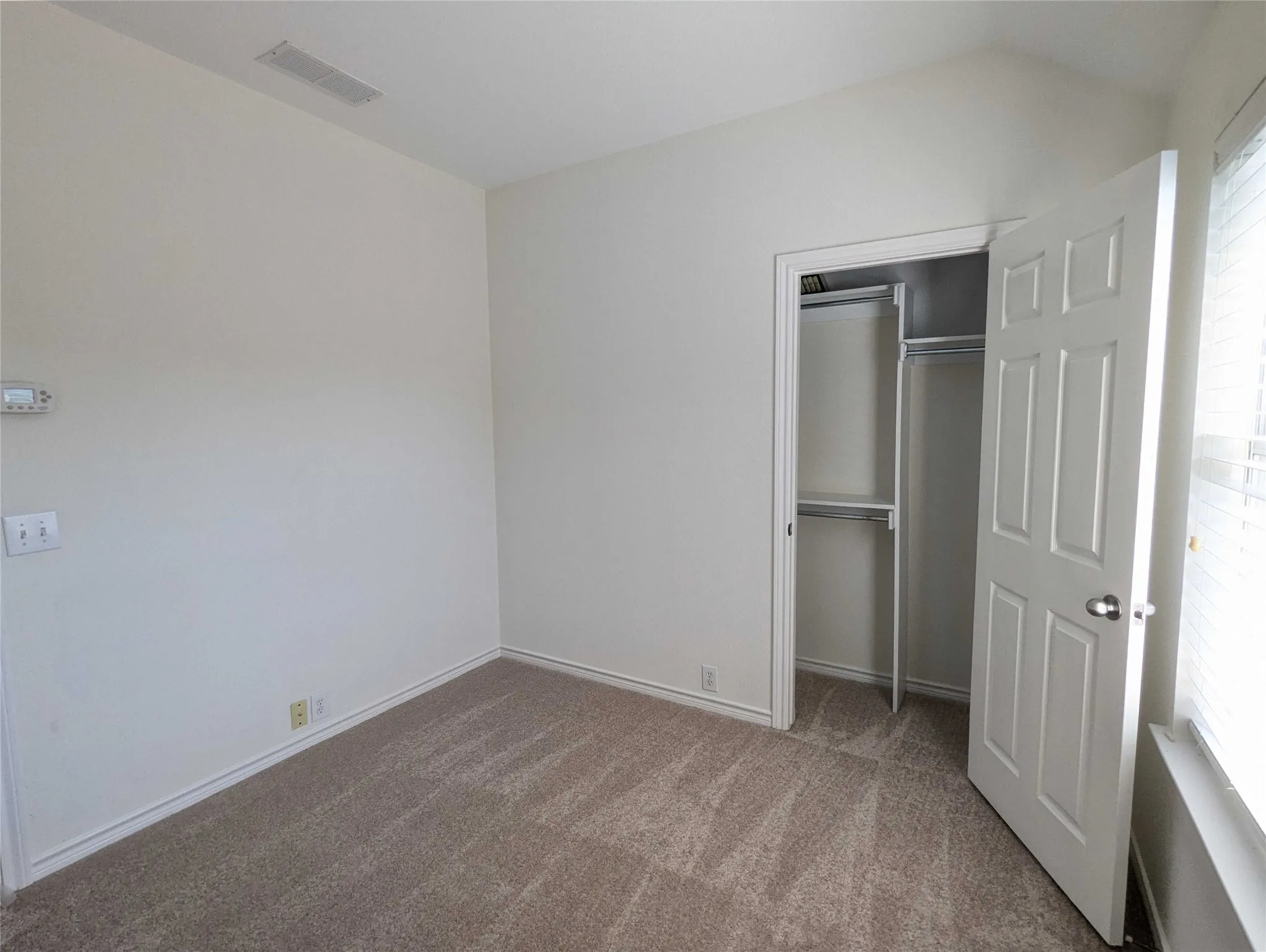 Vaulted ceiling with an integrated vent, light-toned carpeting, and a built-in closet with shelving and hanging rods