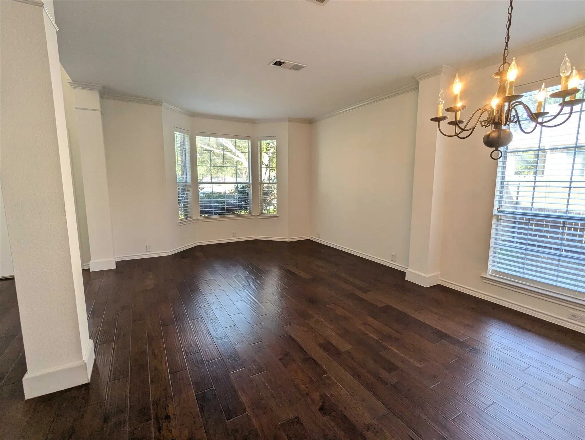 Dark wood-finish flooring, bay window with blinds, decorative chandelier, and white crown molding