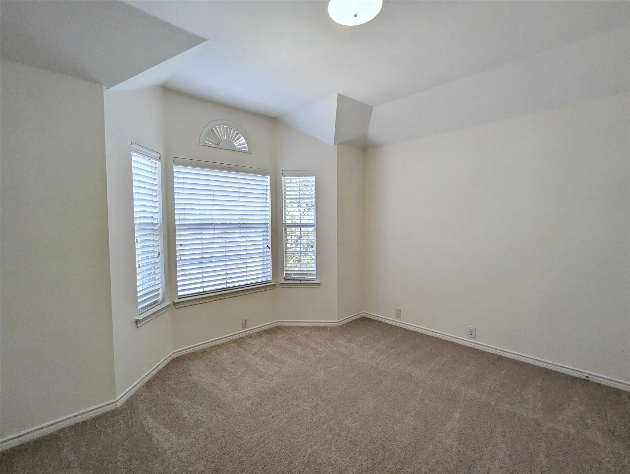 Bay window with arched transom, vaulted ceiling, and neutral carpeting